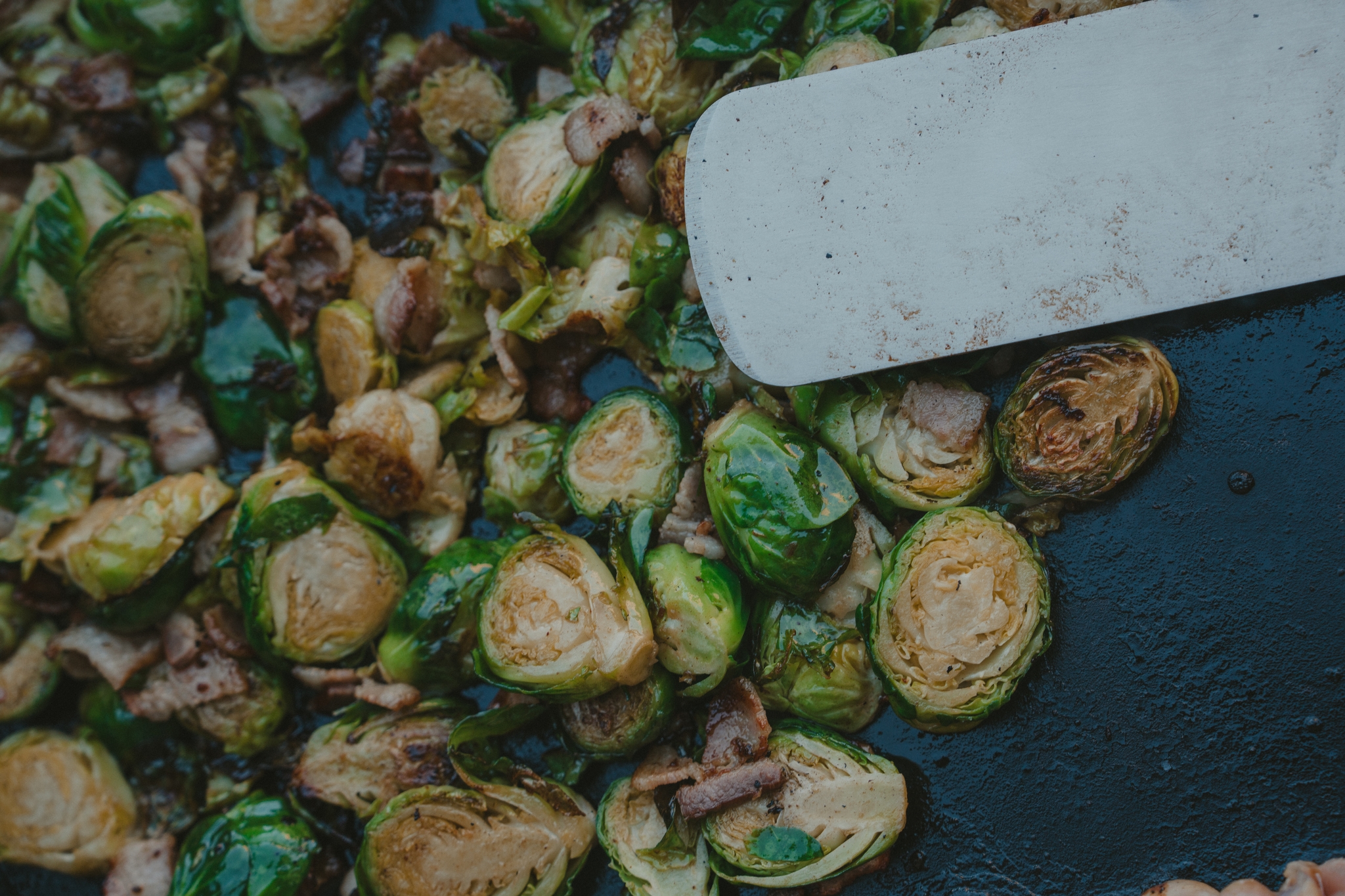 Sliced Brussels sprouts and mushrooms being cooked on a griddle with a spatula