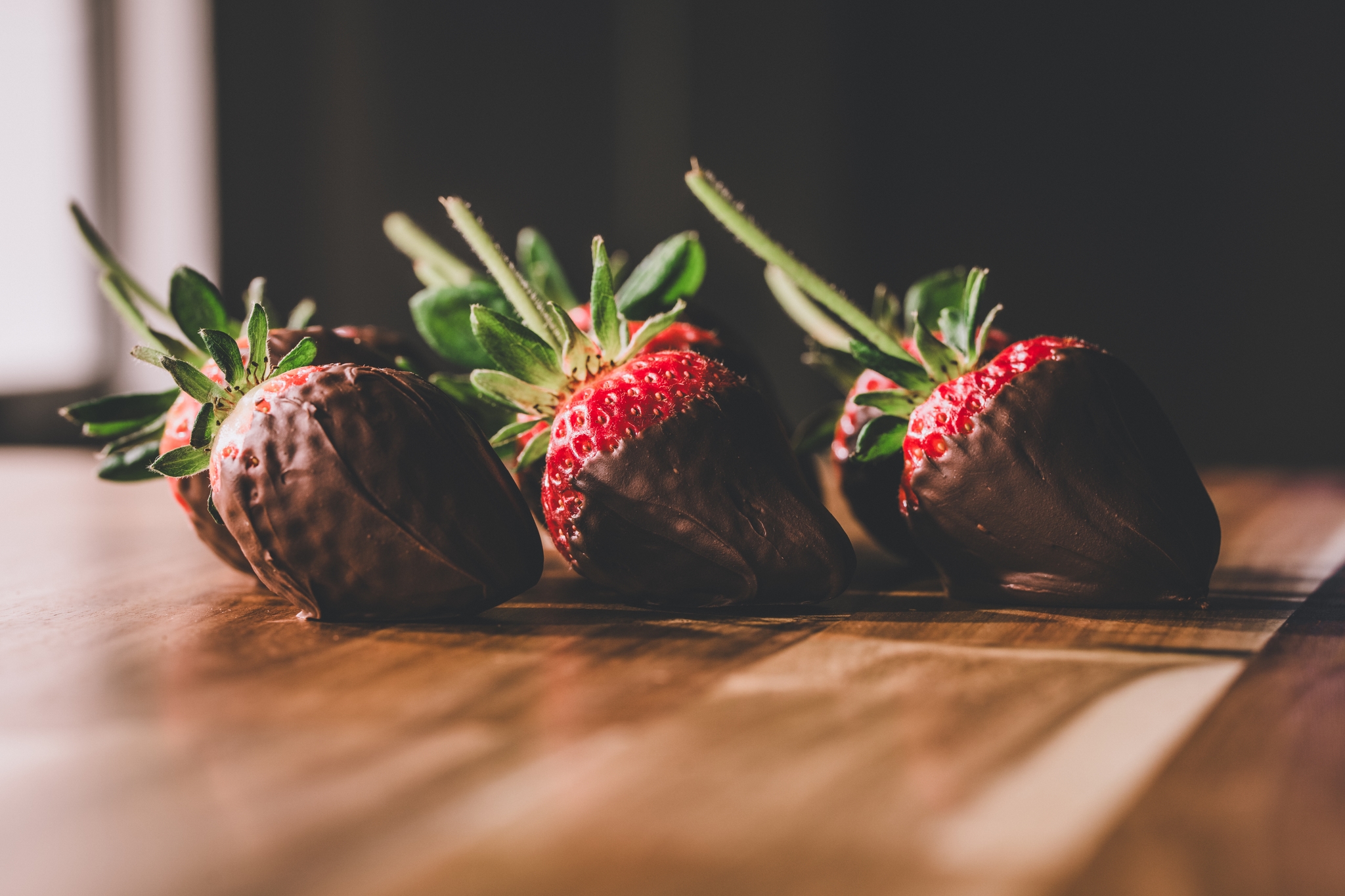 Four strawberries partially dipped in chocolate, arranged on a wooden surface with a soft focus background