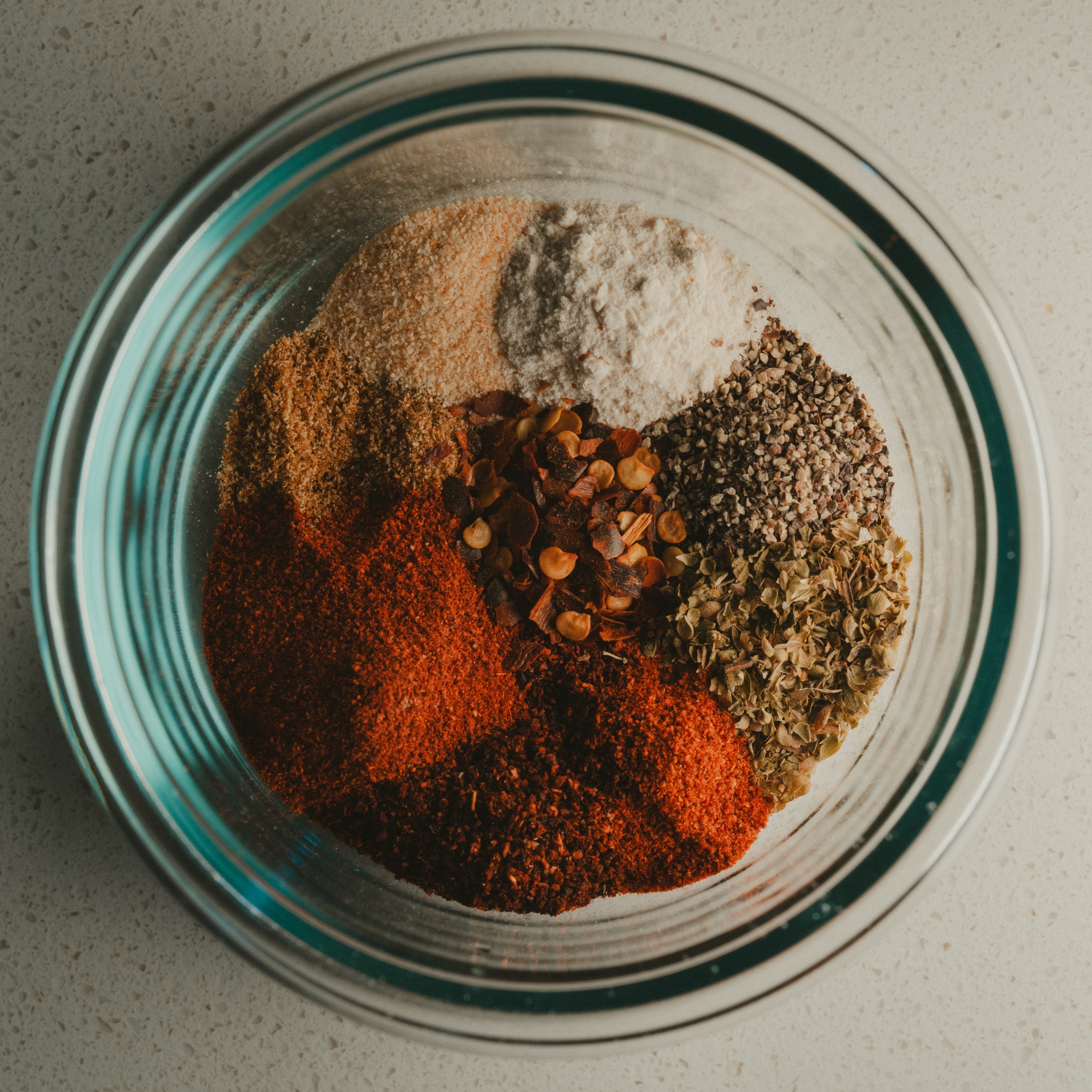 A glass bowl containing various colorful spices arranged in separate sections