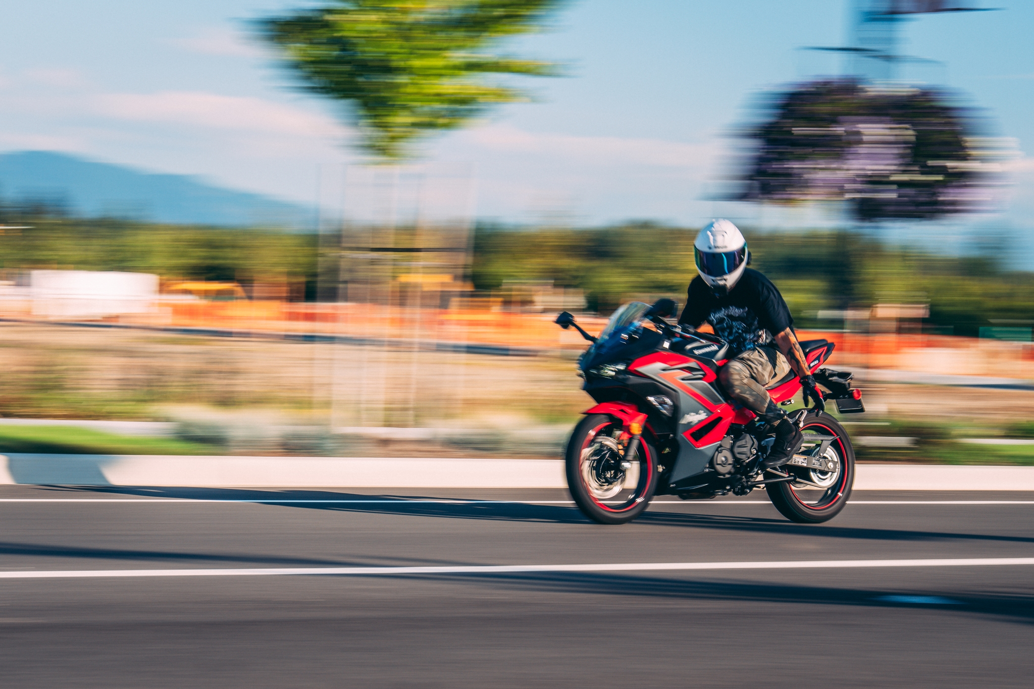 A person wearing a helmet rides a red and black motorcycle at high speed on a road, with a blurred background indicating motion