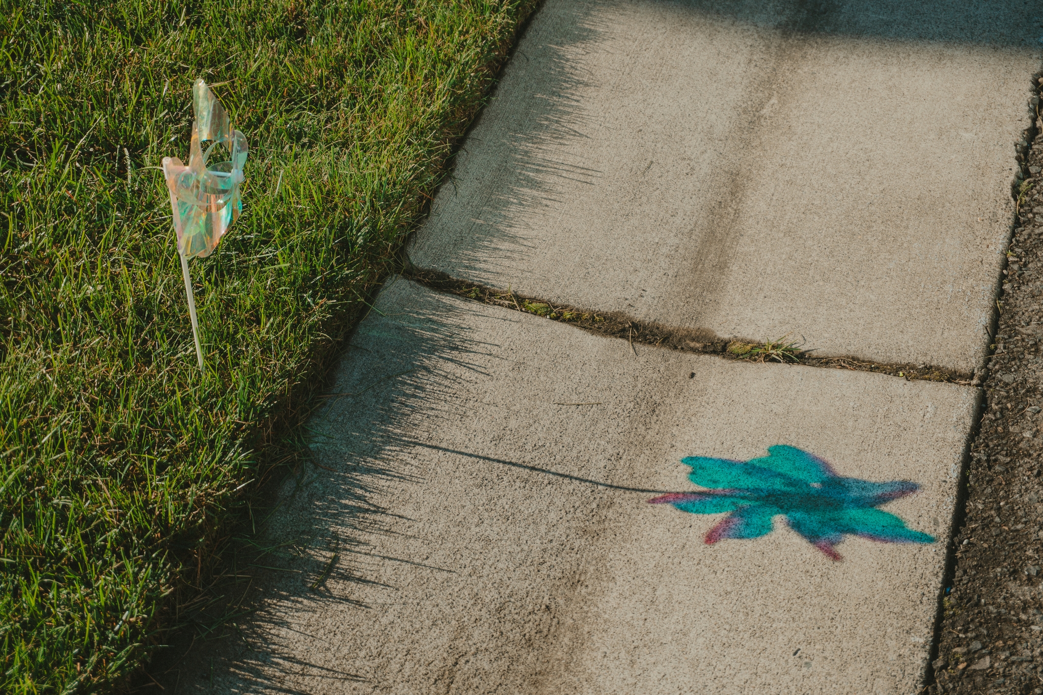 A sidewalk with a painted blue leaf and a small flag on a grassy area nearby