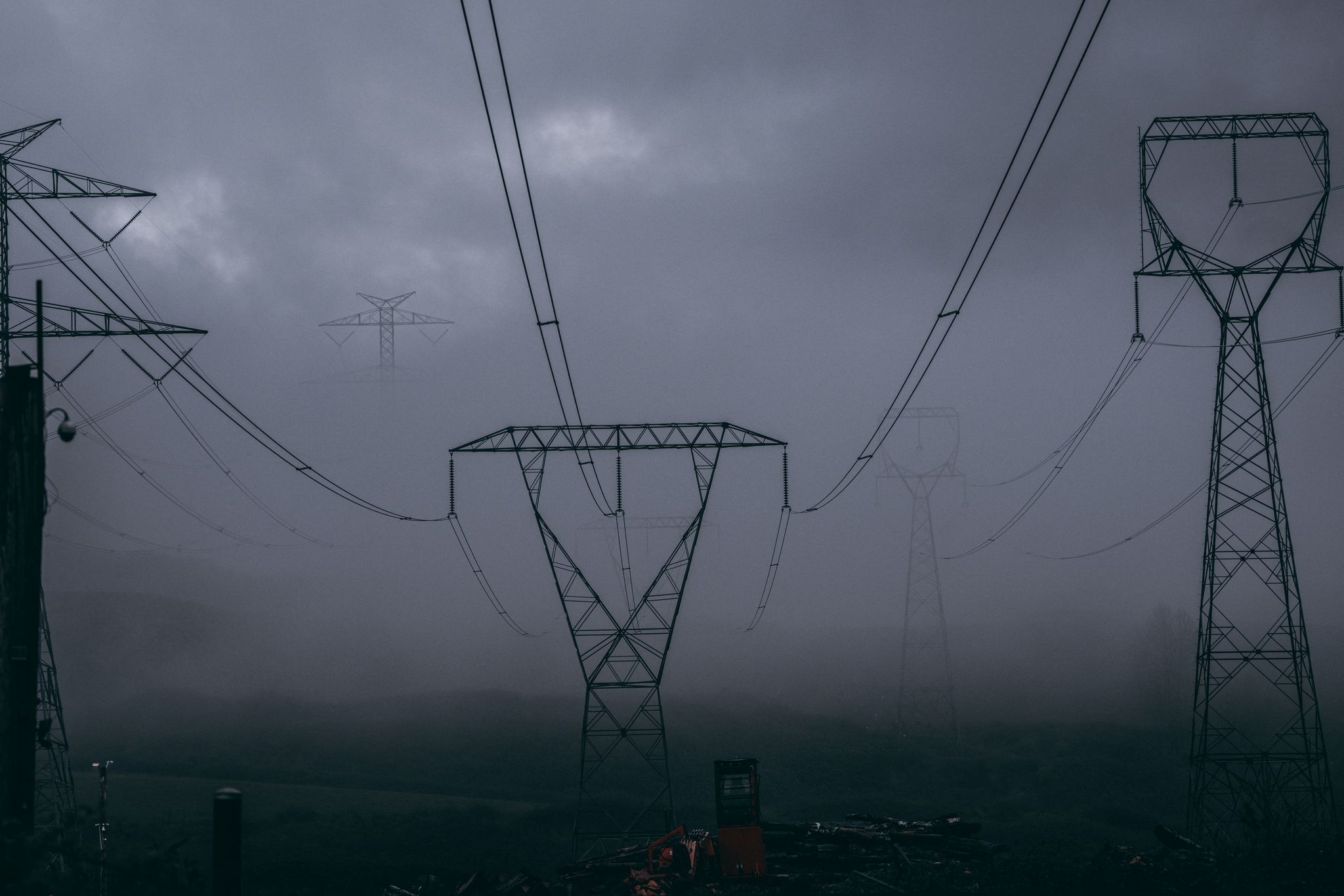 A series of high-voltage power lines and towers silhouetted against a dark, cloudy sky, creating a moody and atmospheric scene