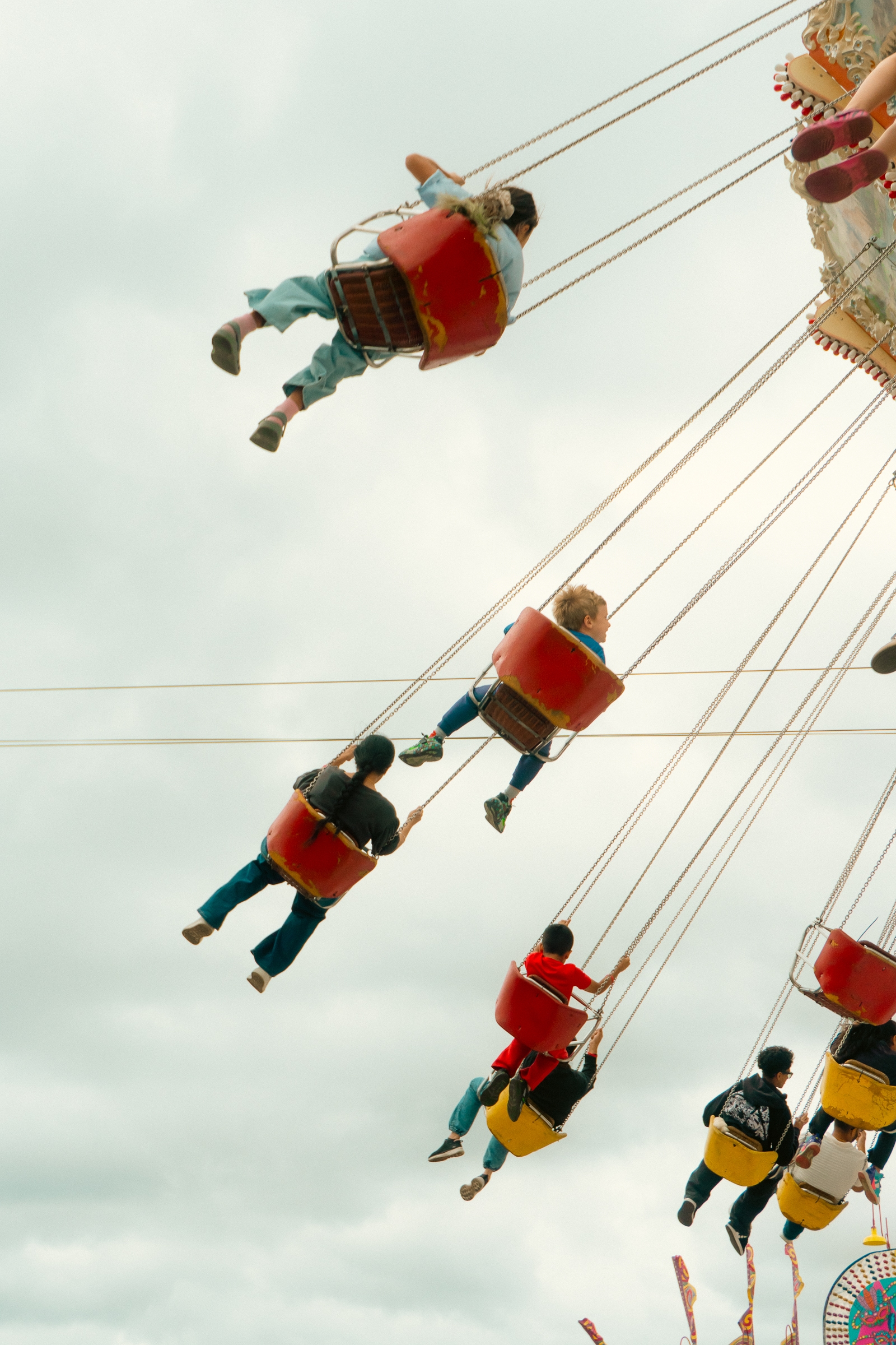 People enjoying a swing ride at an amusement park, suspended high in the air against a cloudy sky