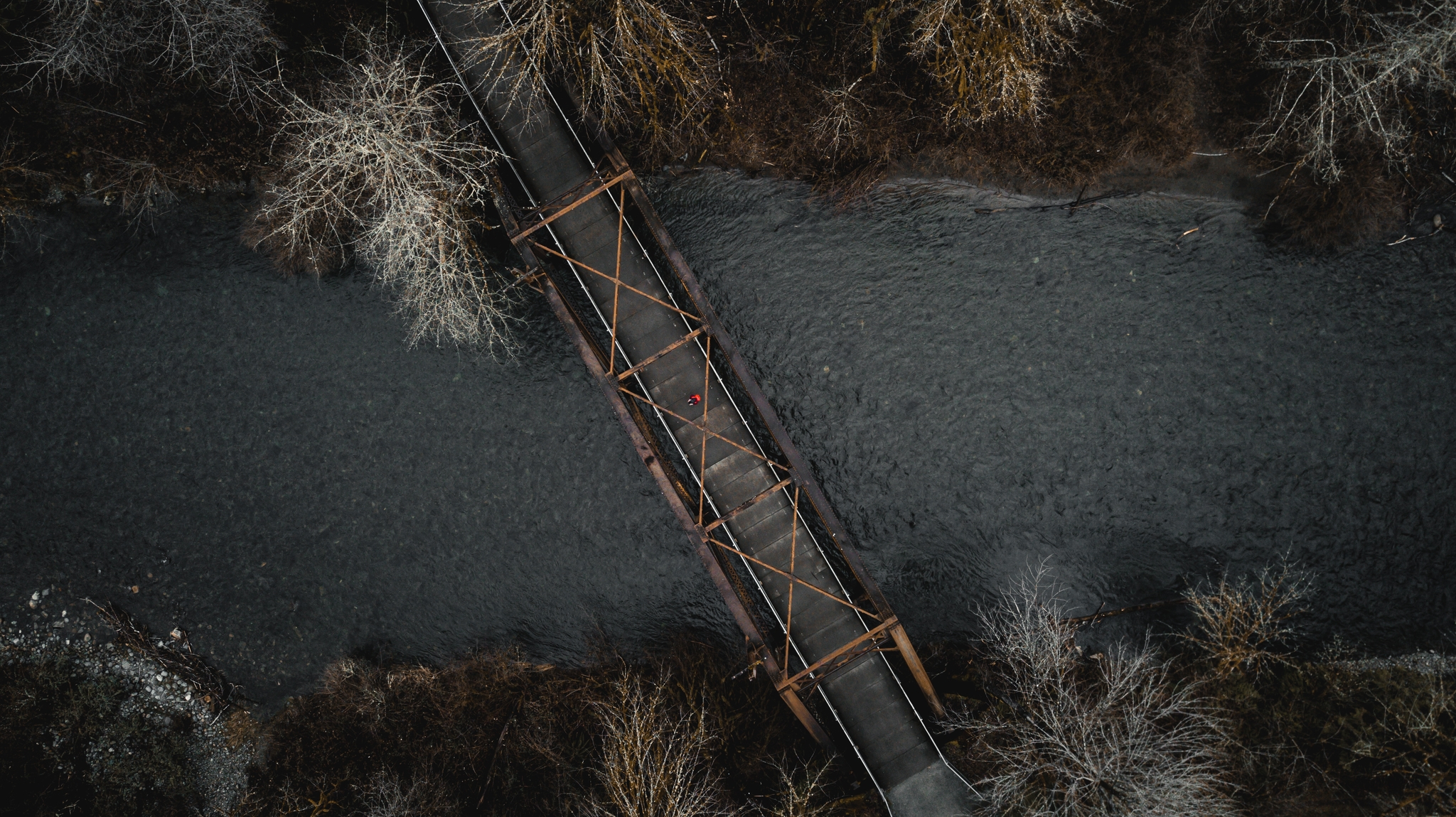 Aerial view of a narrow bridge crossing over a river, surrounded by leafless trees