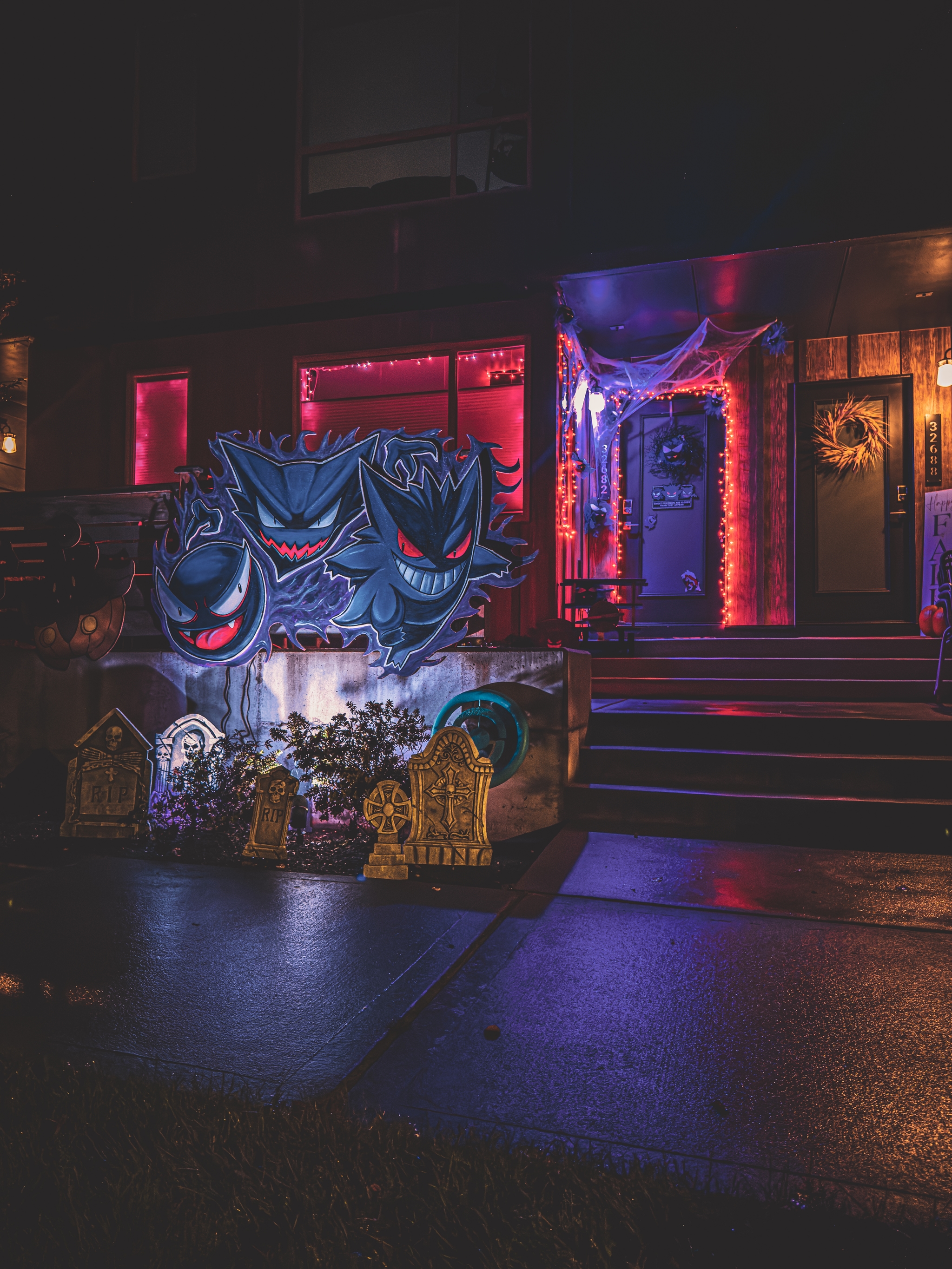 Halloween-themed house with glowing decorations and ghoulish figures in front of steps on a rainy night