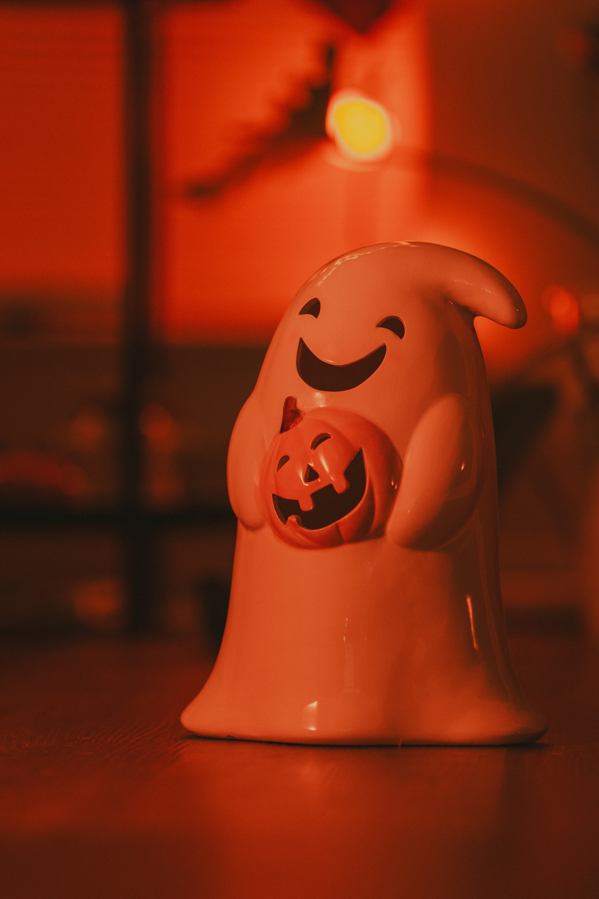 A smiling ceramic ghost holding a pumpkin illuminated by soft orange light