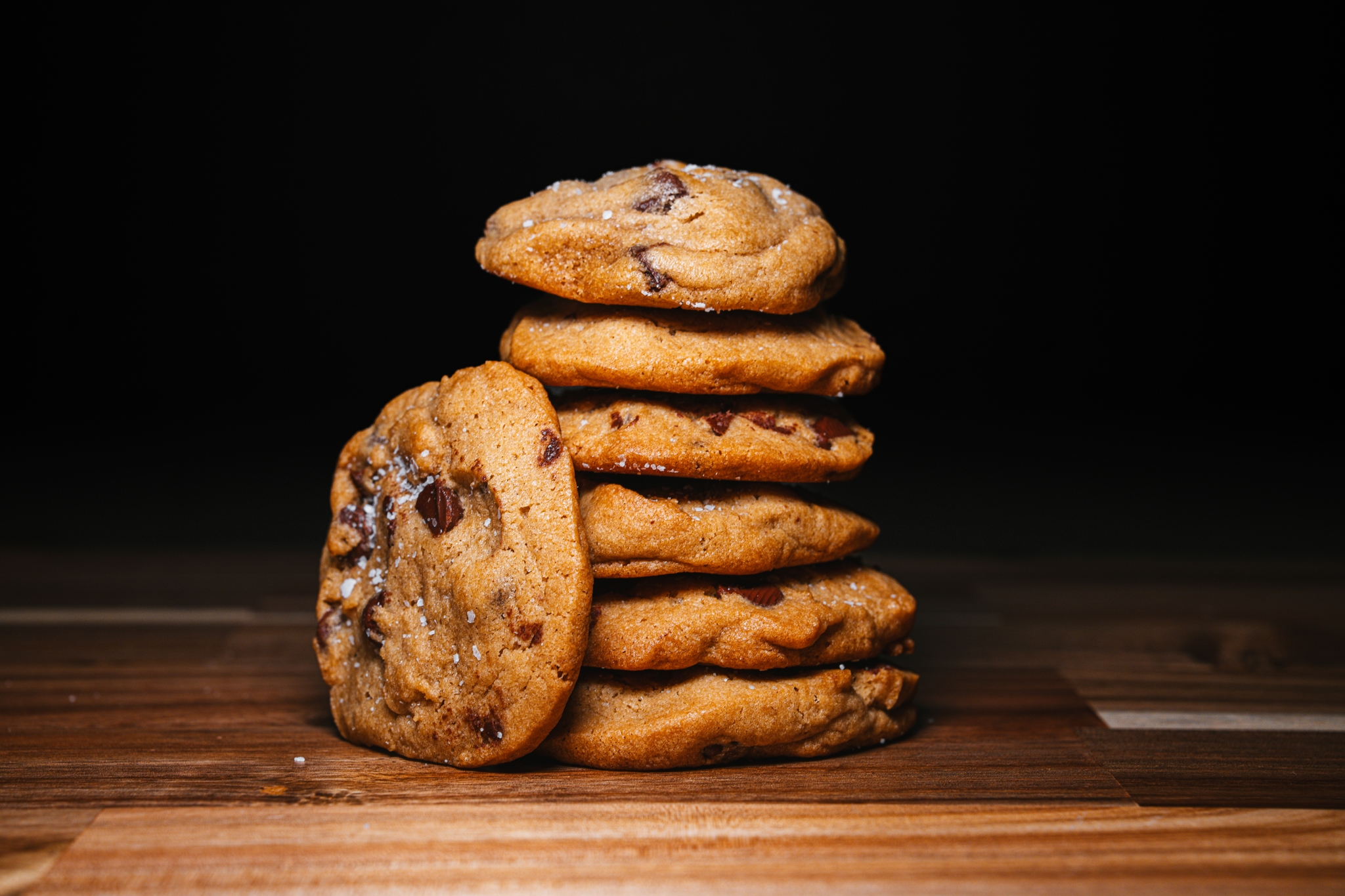 A stack of chocolate chip cookies on a wooden surface against a dark background