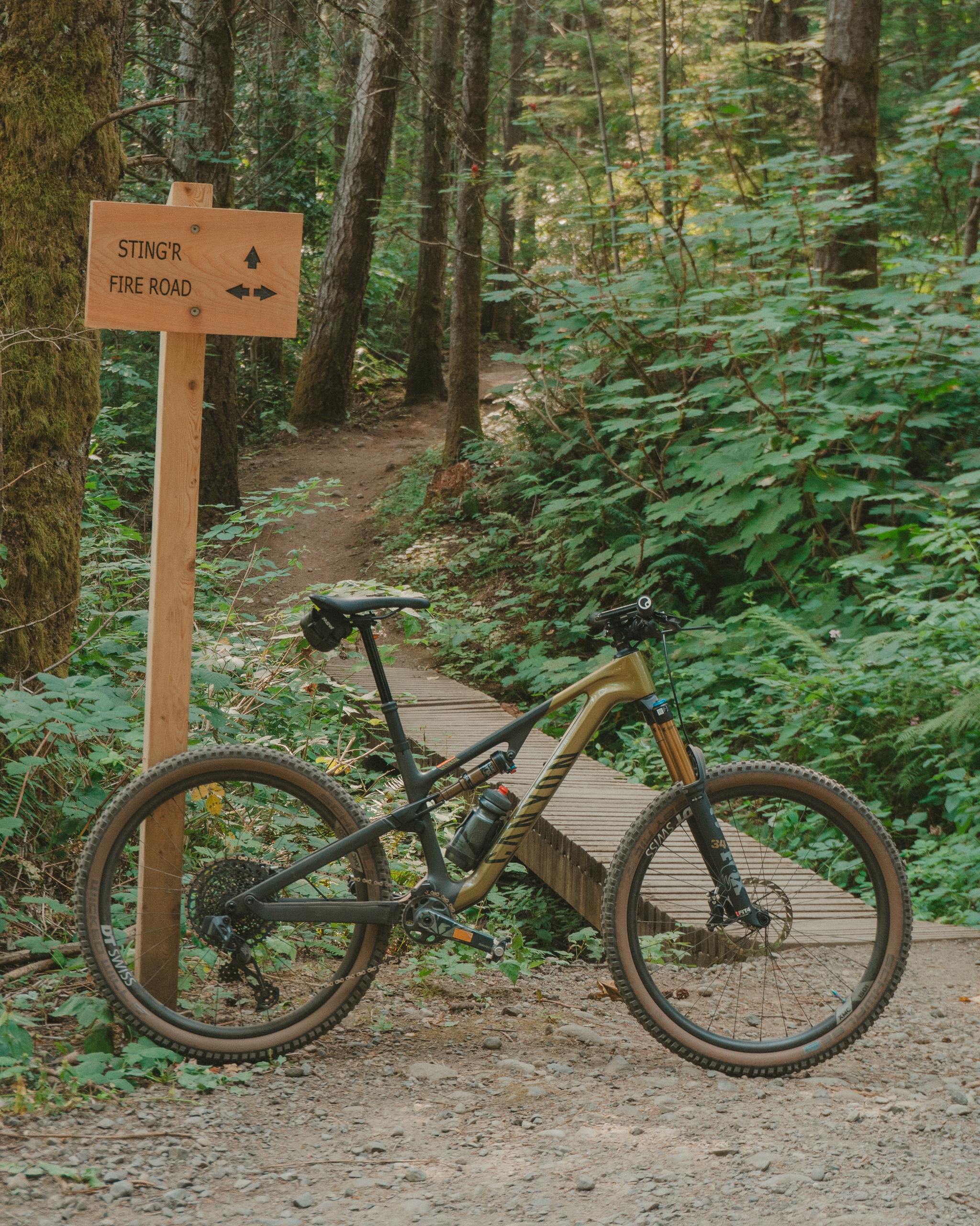 A mountain bike is parked on a forest trail next to a wooden signpost