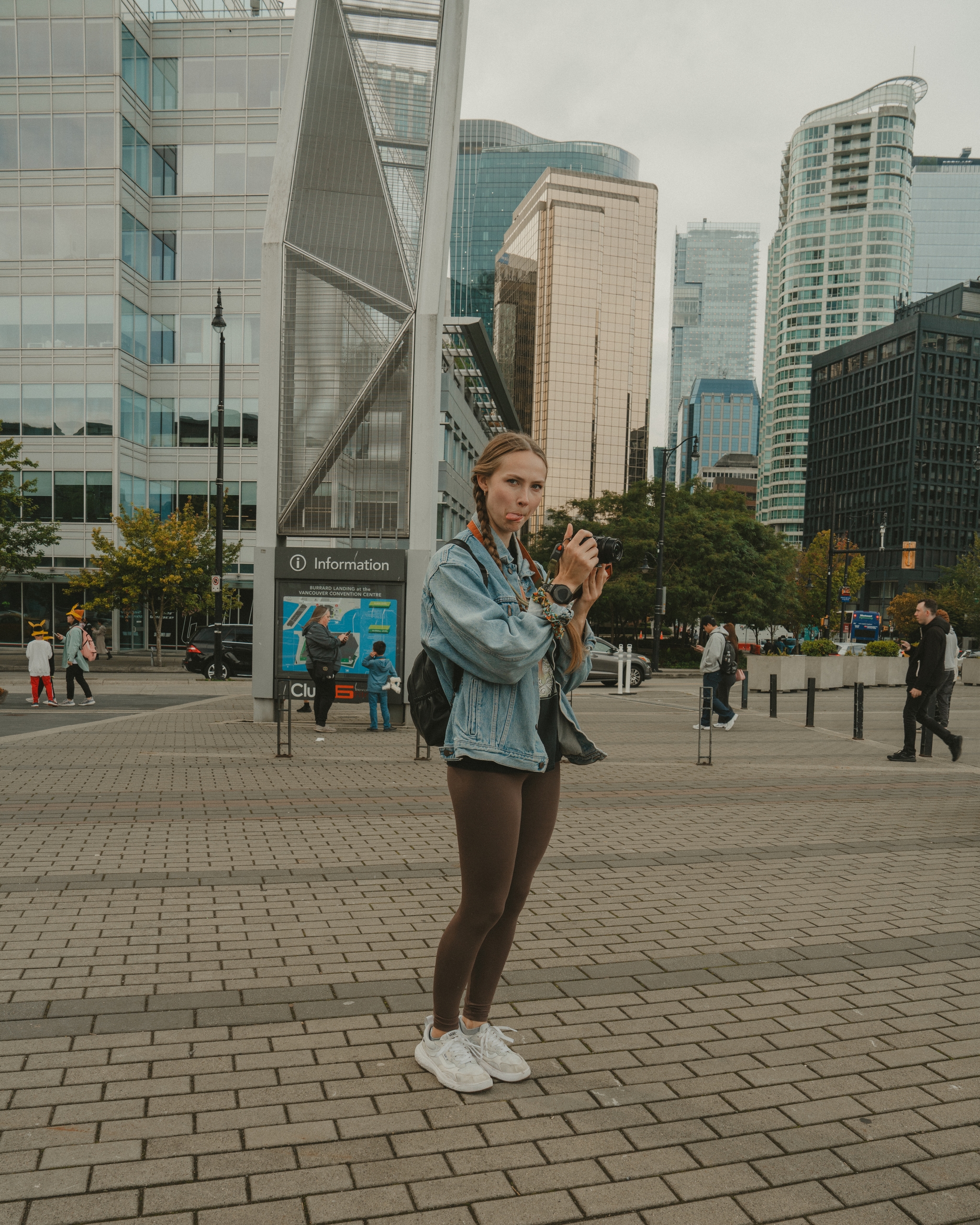 An individual with a camera stands in a city plaza surrounded by modern architecture and skyscrapers