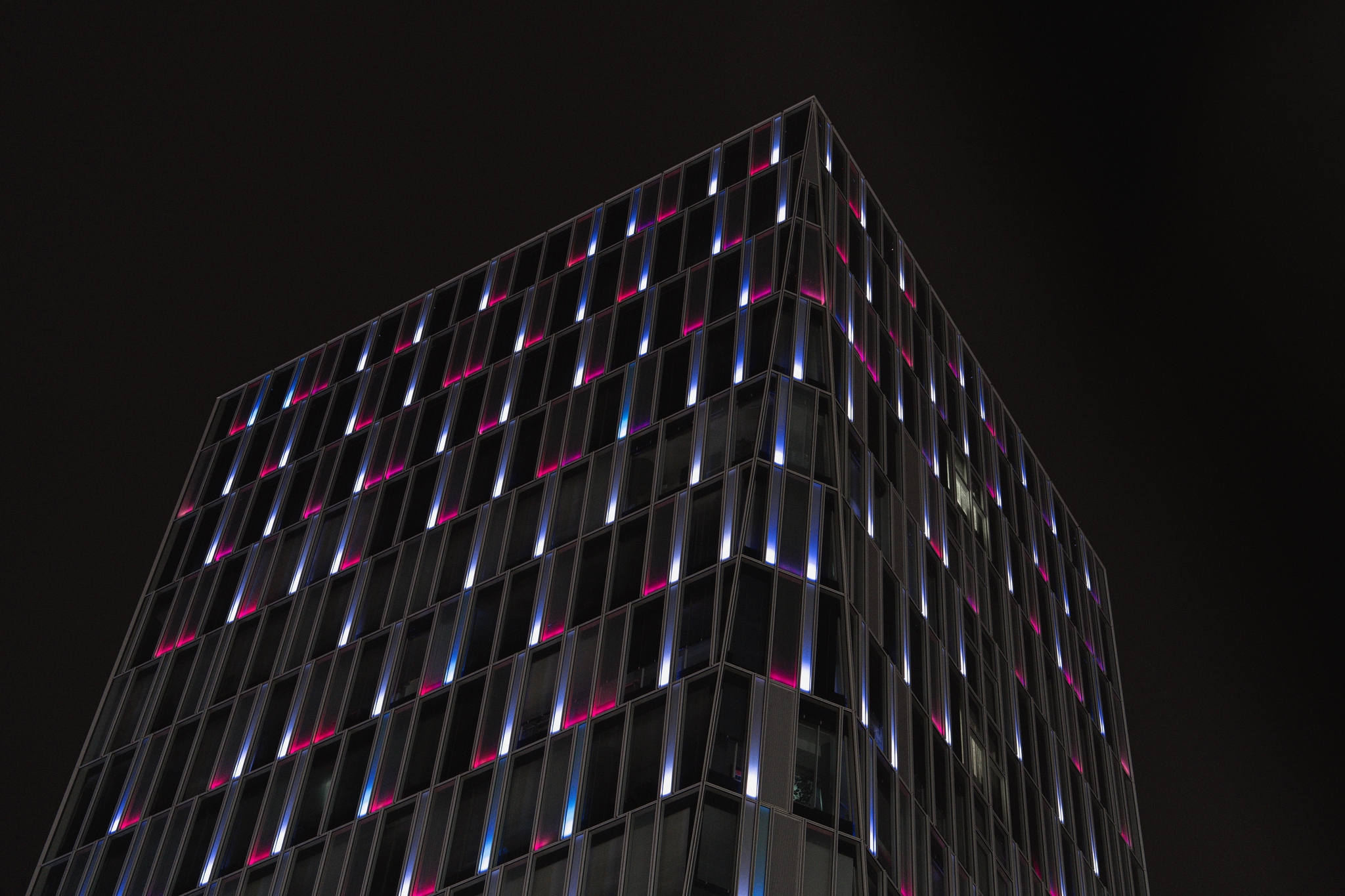 A building with a grid-like facade illuminated by colorful lights against a dark sky