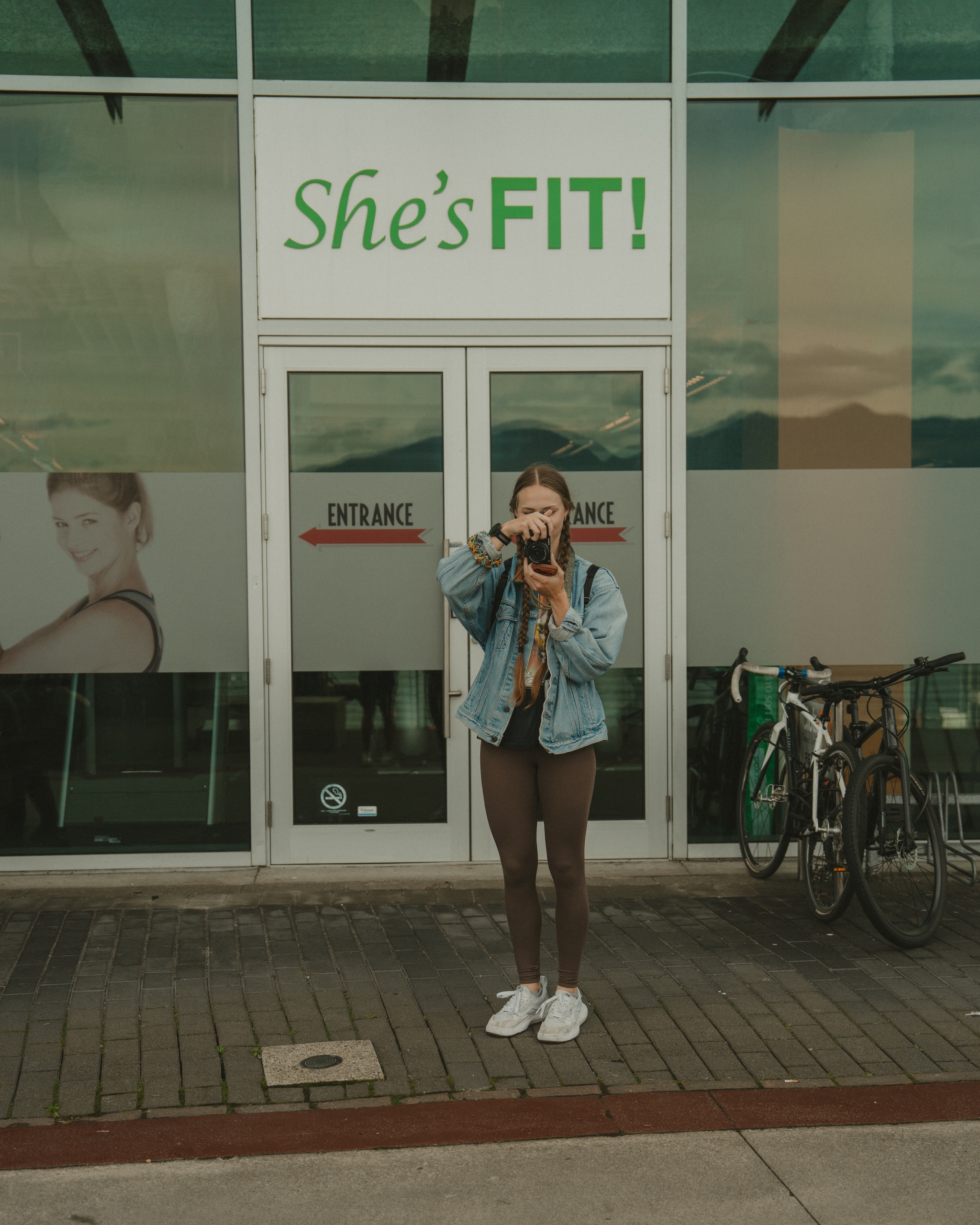 Woman photographing in front of fitness studio with bicycle nearby