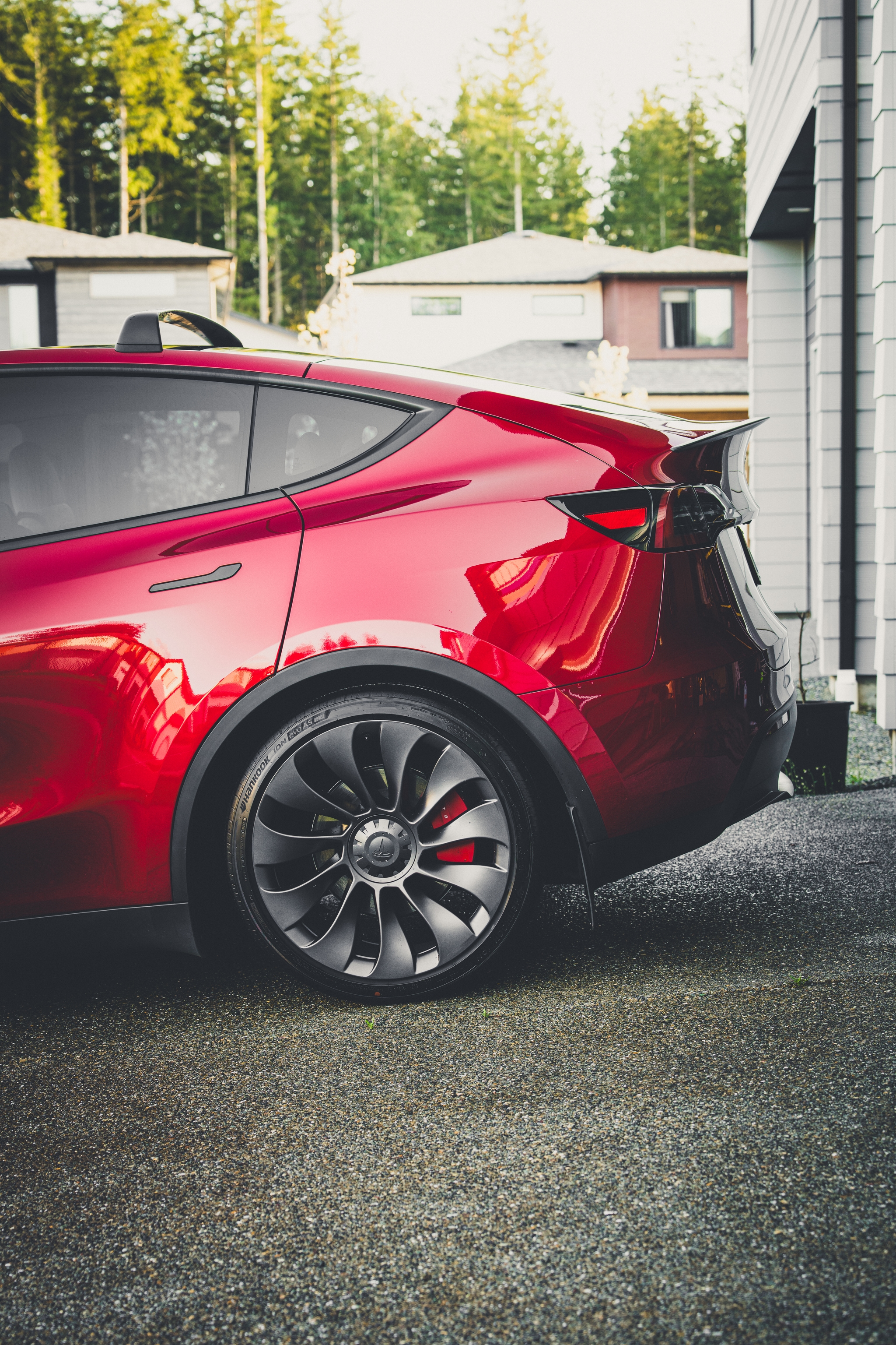 A red tesla model y performance parked on a driveway, with modern houses and trees in the background