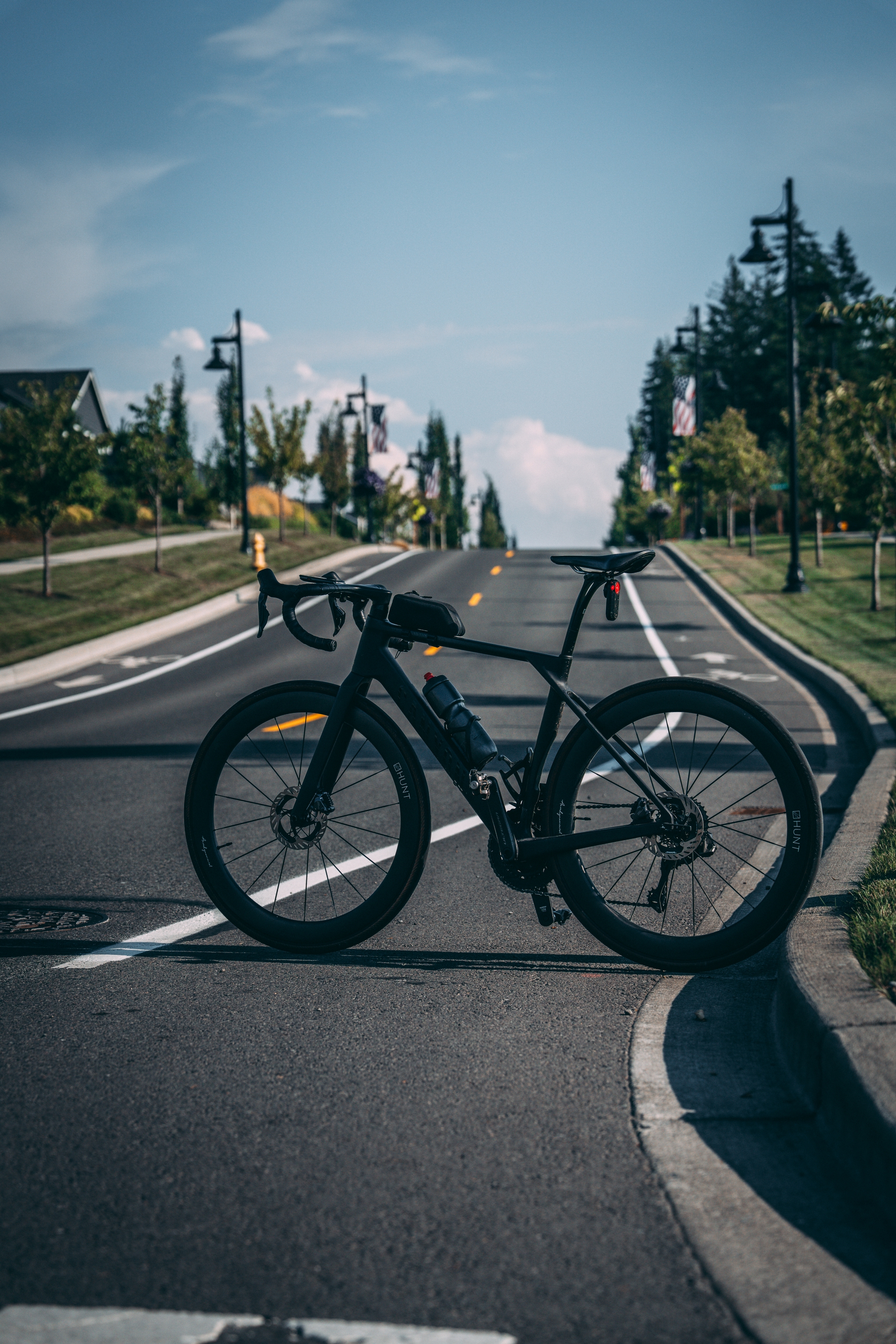A bicycle is parked on a road with a clear sky and trees lining the street