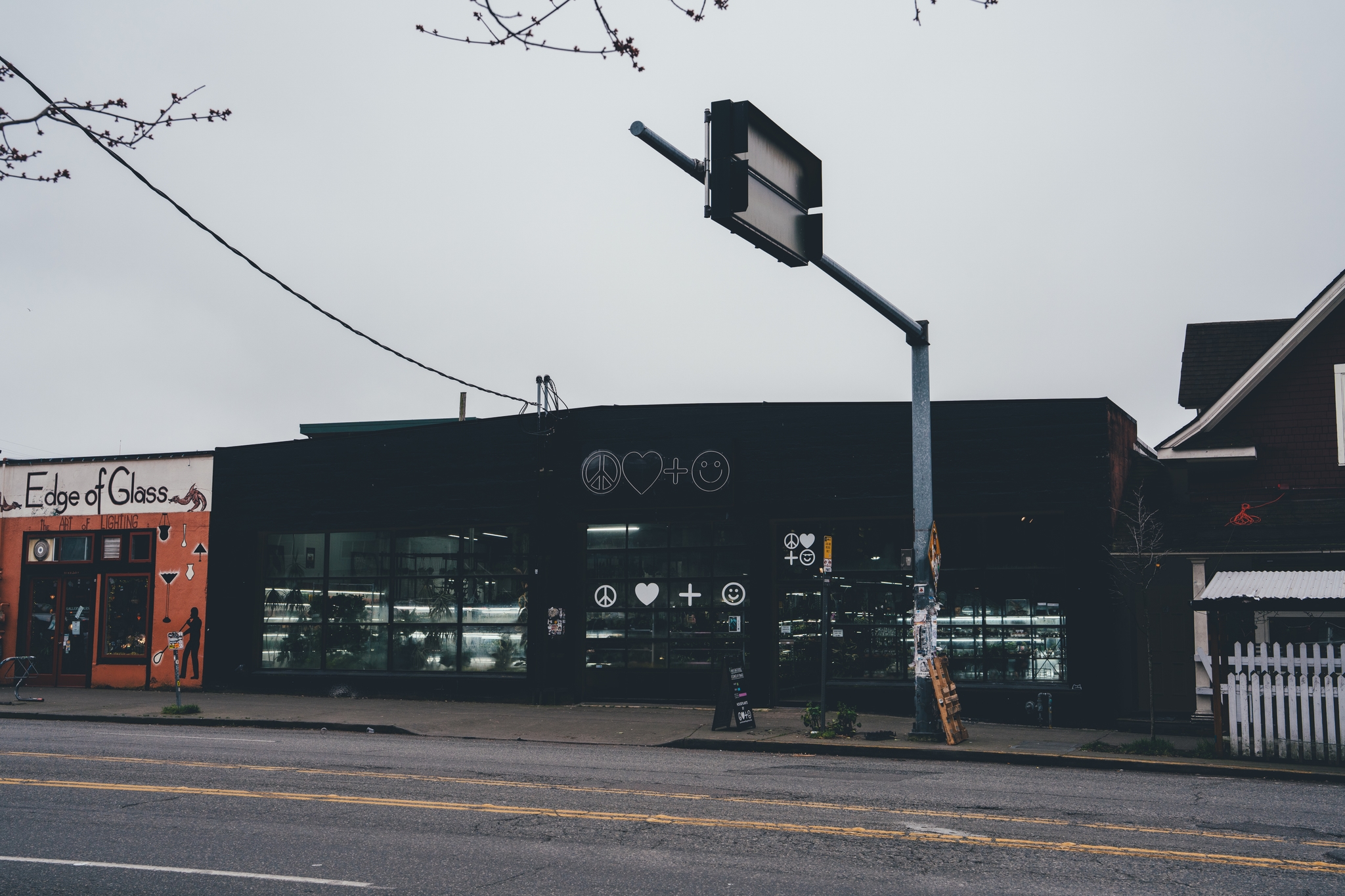 A street scene featuring a row of buildings, including a black storefront with large windows and a red building to the left A traffic light and power lines are visible above the street
