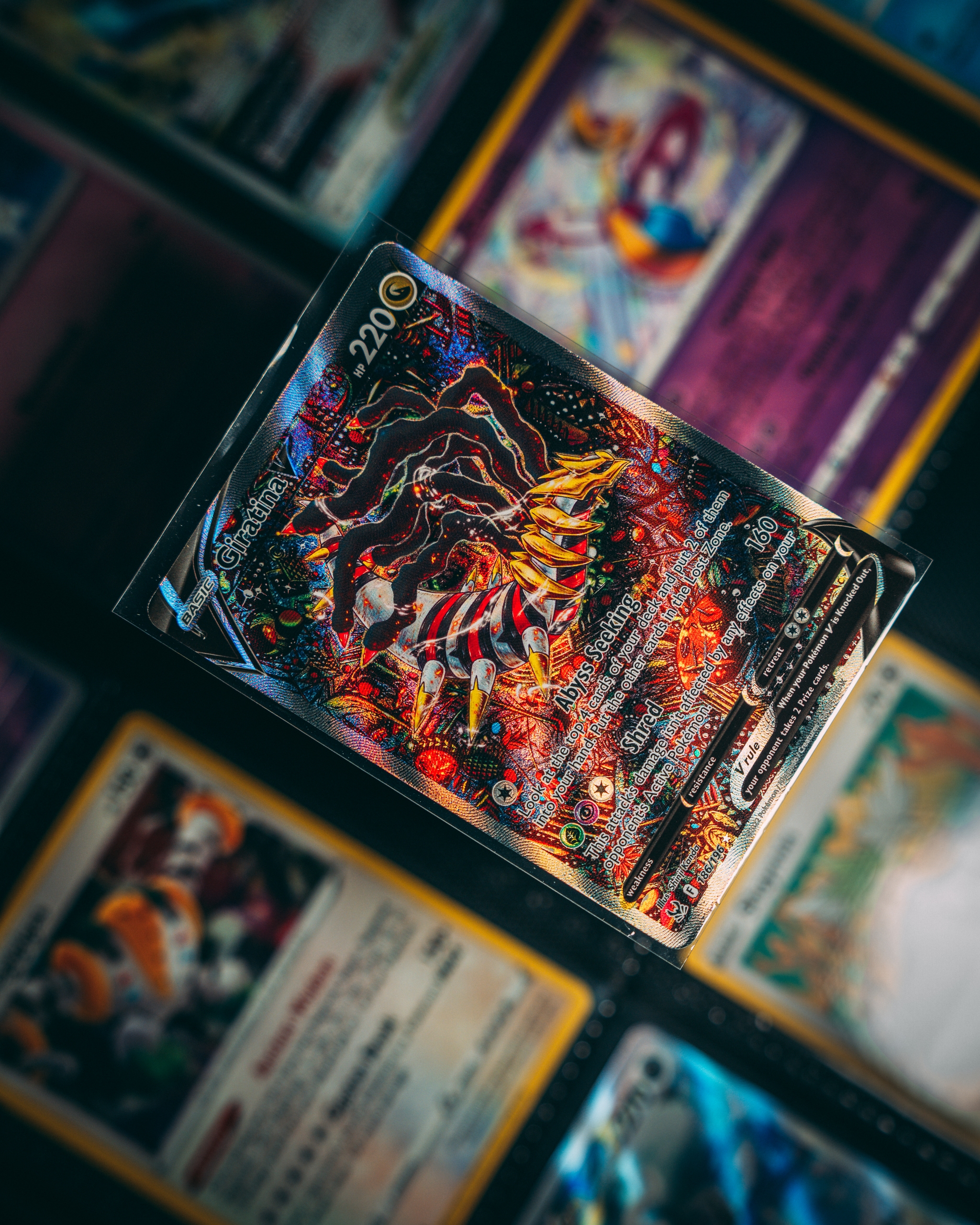 A collection of trading cards with a focus on one card in a protective sleeve. The central card features vivid colors and intricate design elements, surrounded by other cards with various illustrations and text