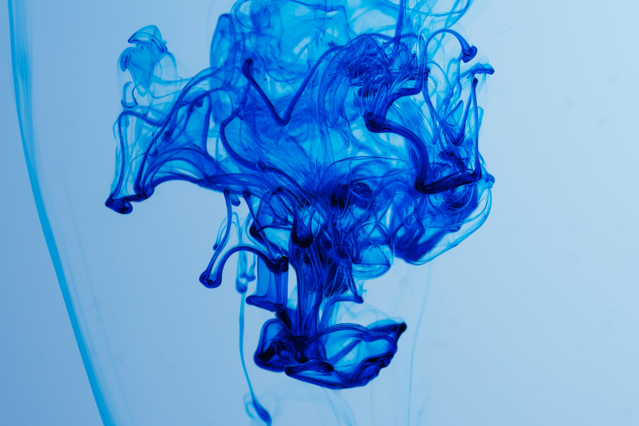 Blue ink swirling in water, creating abstract patterns against a light background