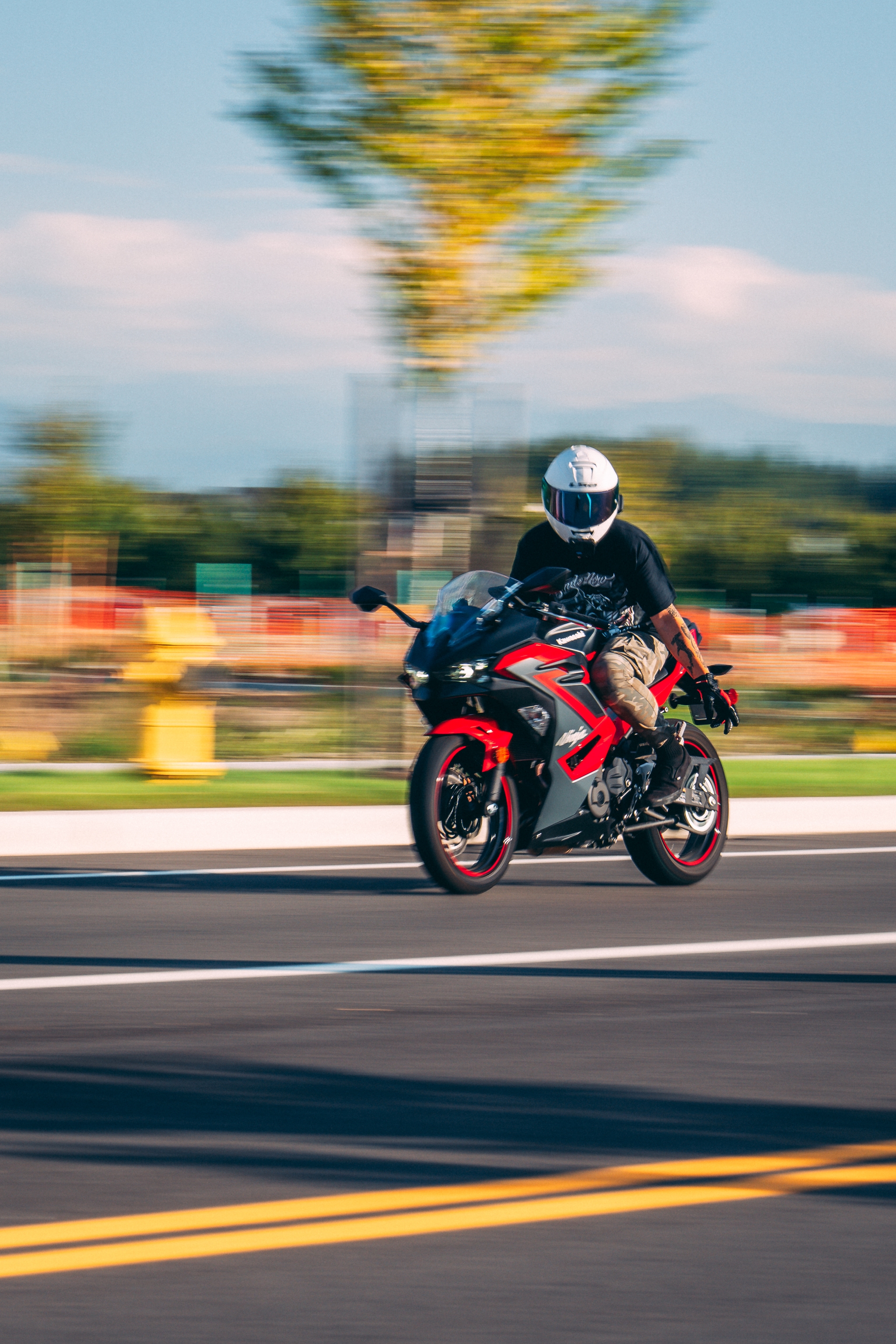 A motorcyclist wearing a helmet rides a red and black sports bike on a paved road, with a blurred background indicating speed