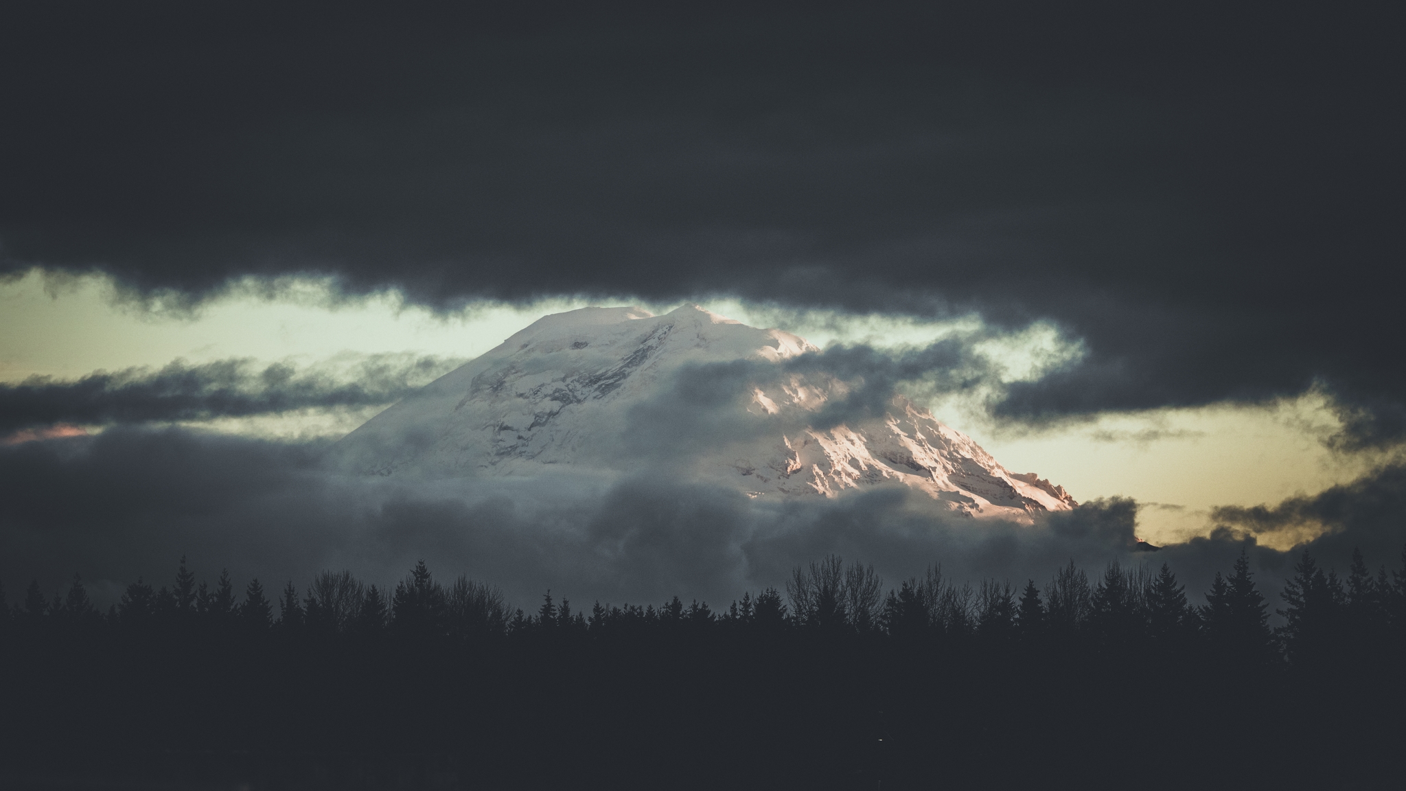 A snow-capped mountain peak partially revealed by moving clouds with dark atmospheric tones