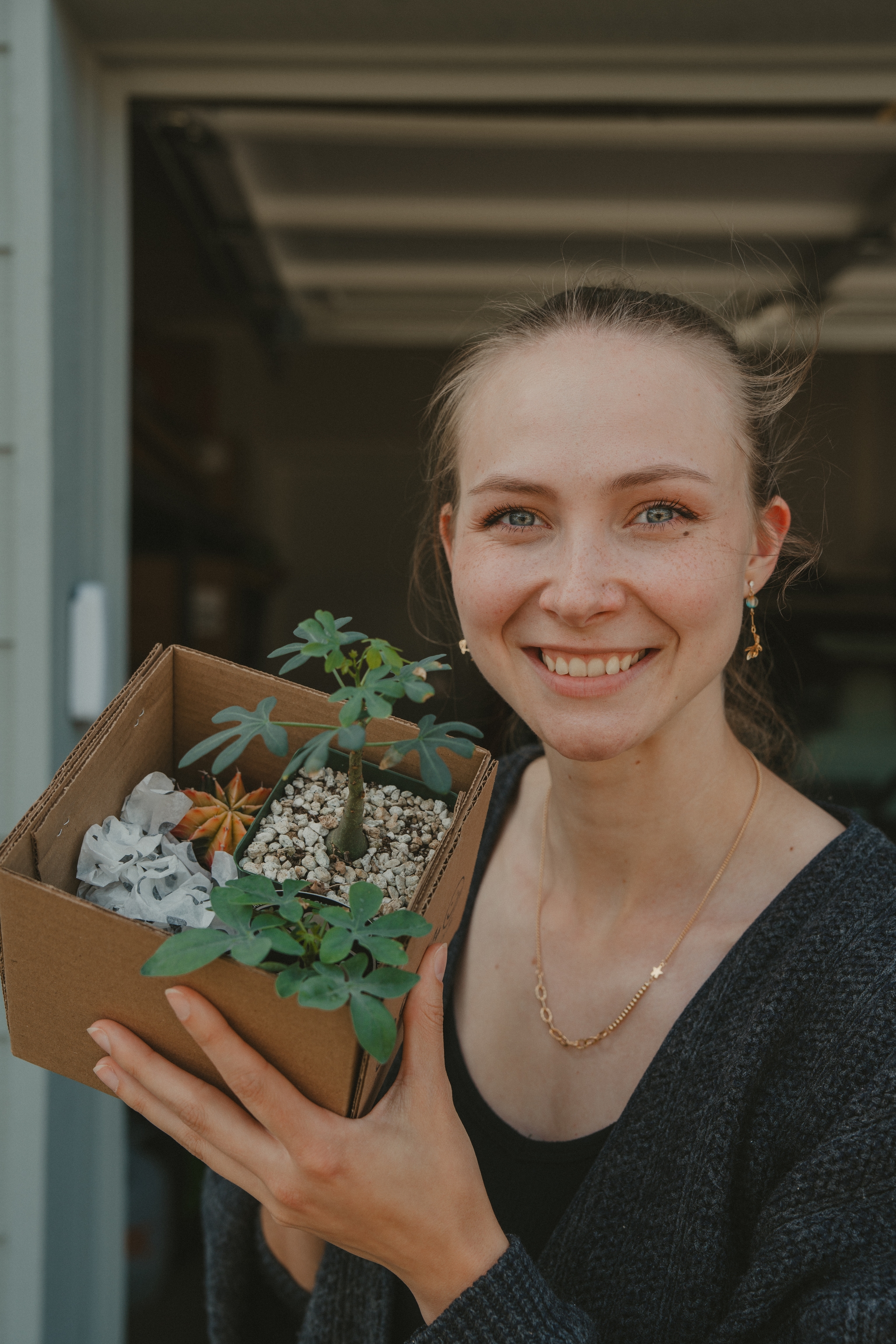 A person smiling and holding a cardboard box containing small plants