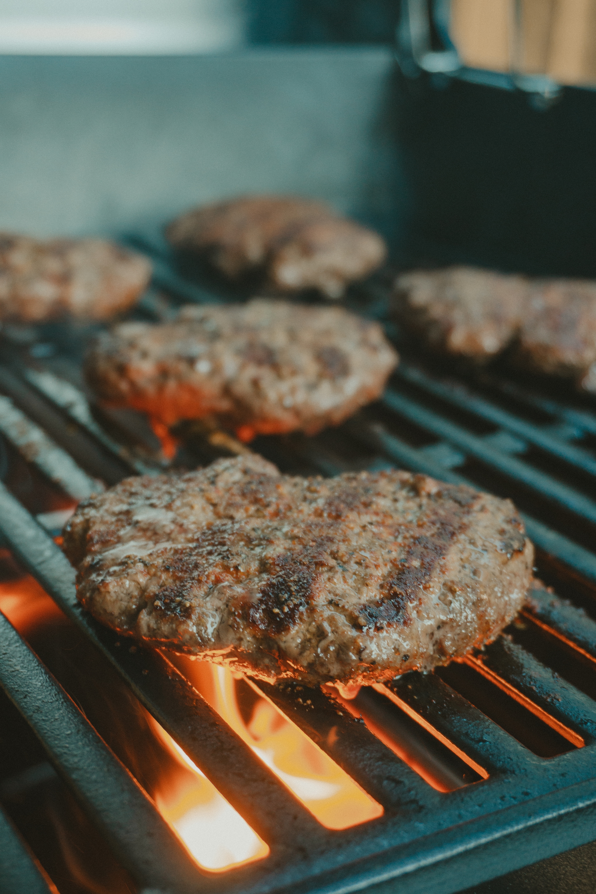 Hamburger patties cooking on a grill with visible flames beneath