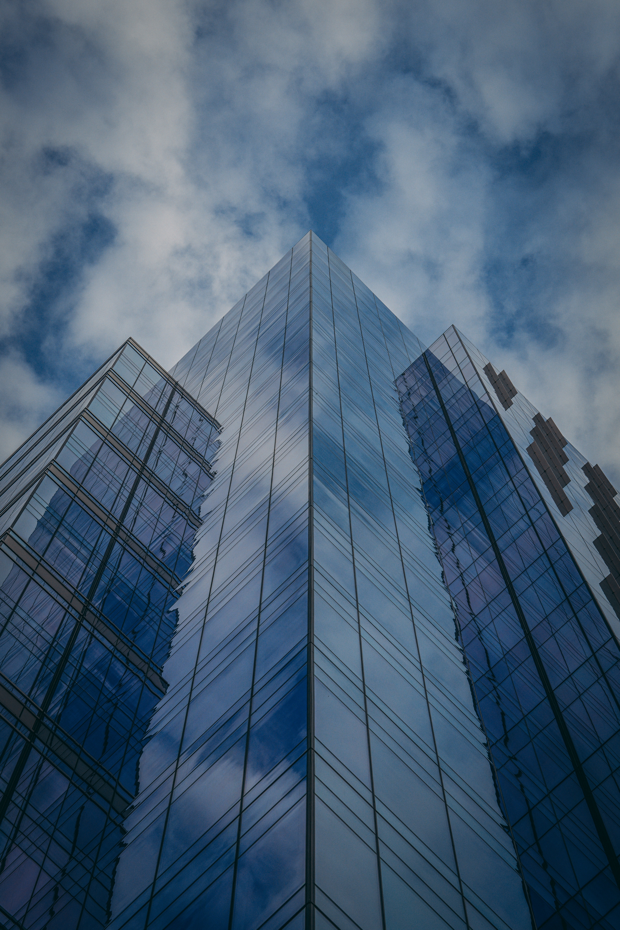 A tall, modern glass skyscraper reflecting the cloudy sky, viewed from a low angle