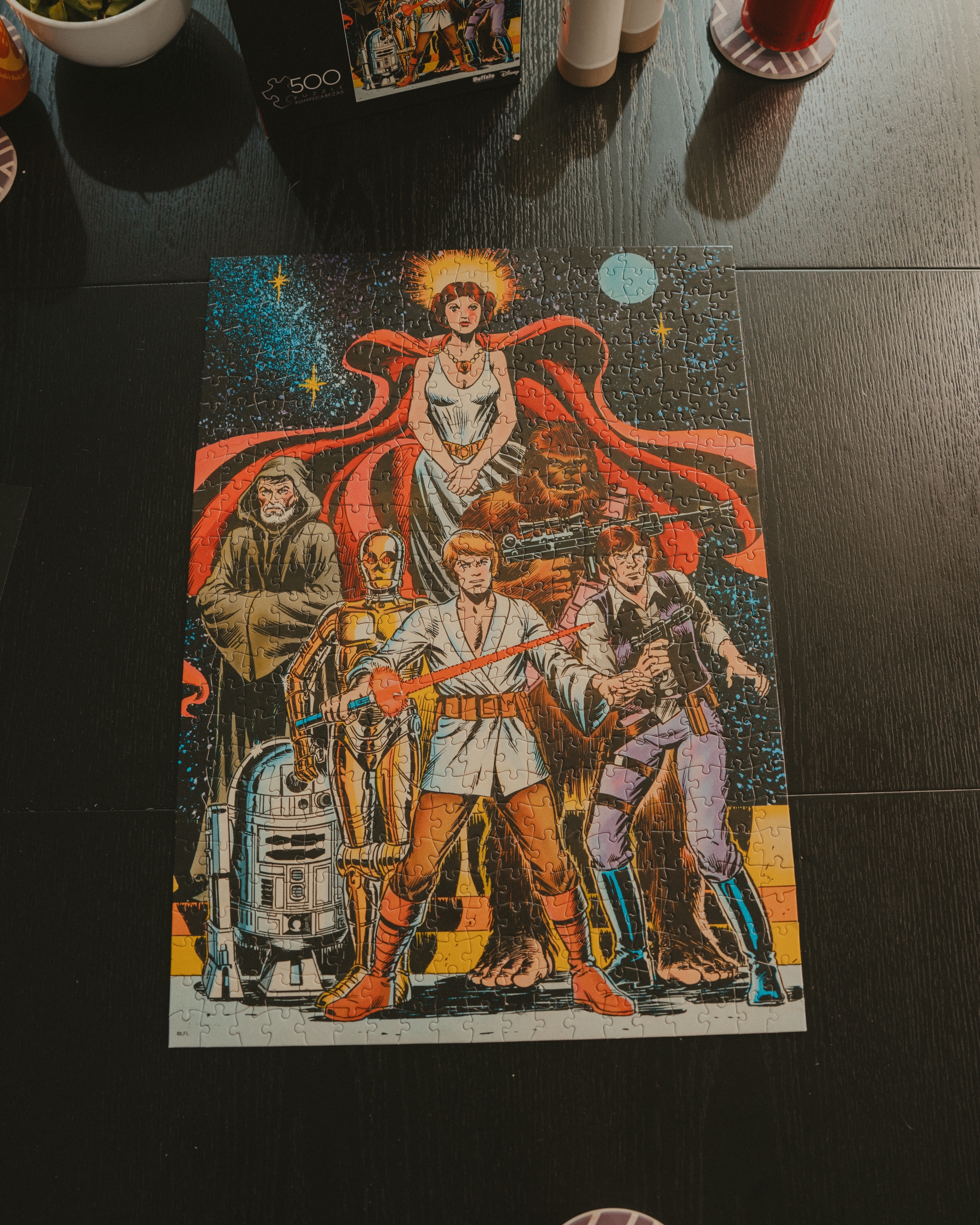 completed vintage style Star Wars poster puzzle laid out on a dark tabletop with surrounding household items at the edges