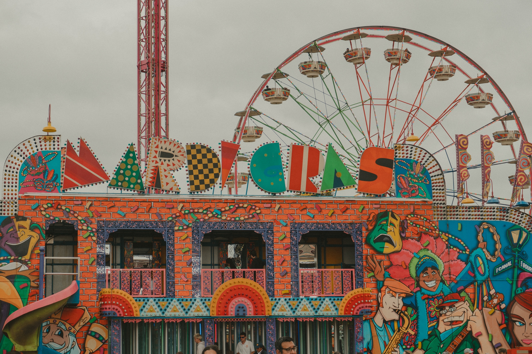 A colorful carnival entrance with vibrant lettering and artwork, alongside a Ferris wheel in the background