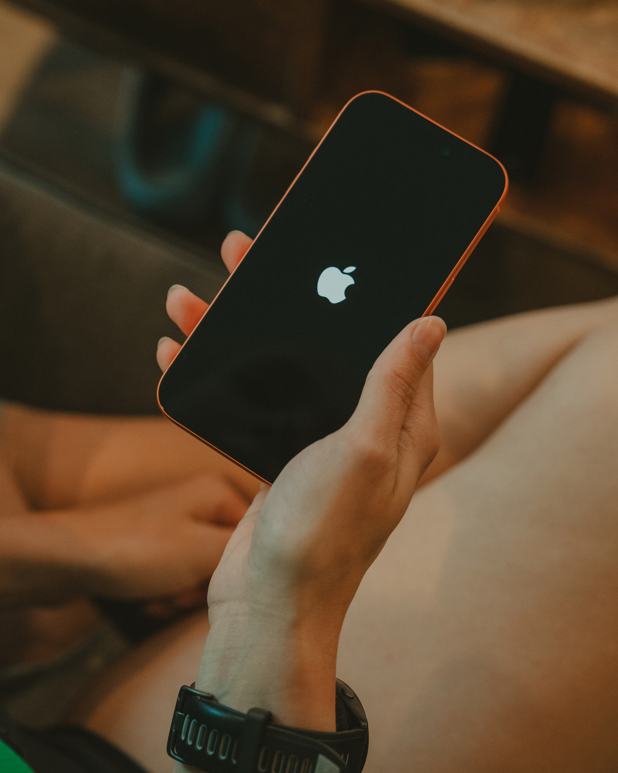 A hand holding a black smartphone with the Apple logo on the screen, alongside a wristwatch on the person's arm