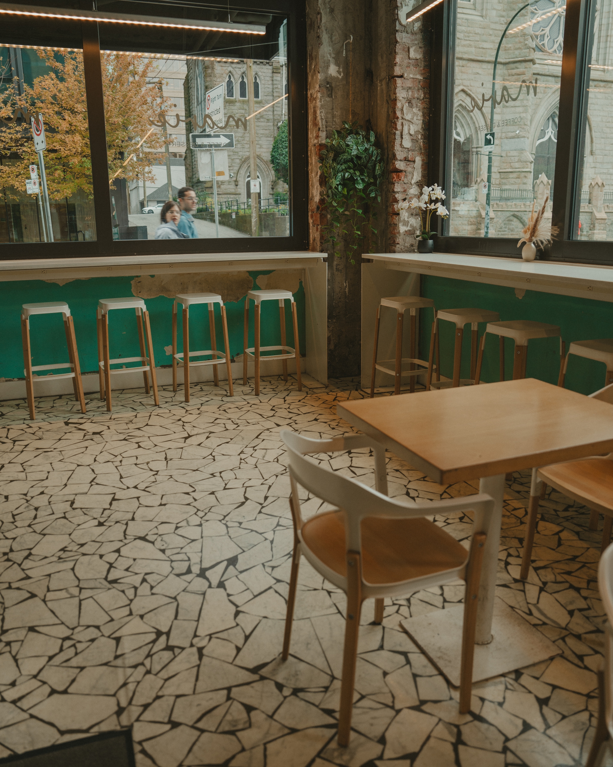 Modern cafe interior with mosaic floor, wooden tables, and high stools by a large window