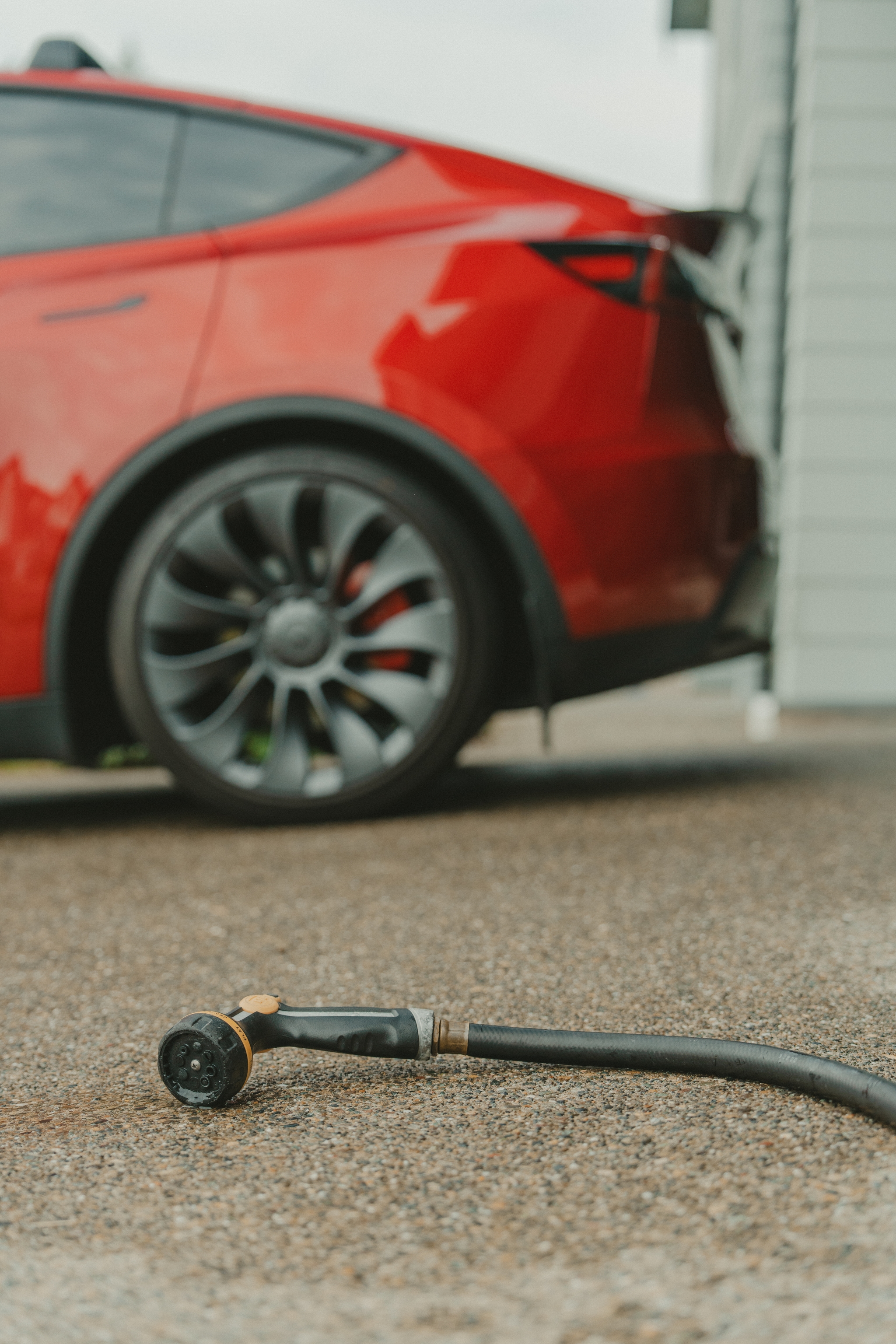 A red car parked on a wet driveway with a garden hose lying on the ground in the foreground