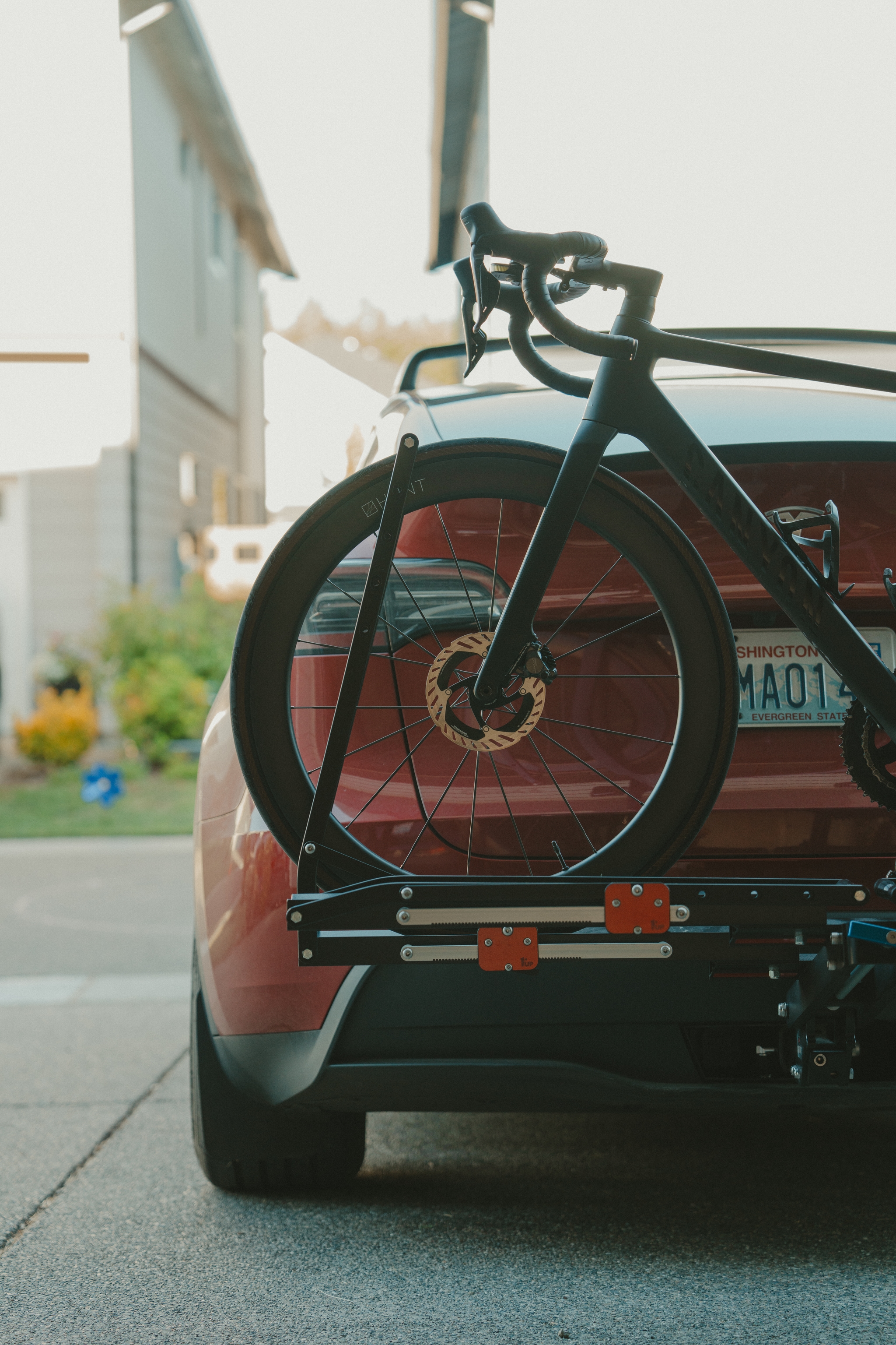 A red car with a bicycle mounted on a rear bike rack, parked in a residential driveway