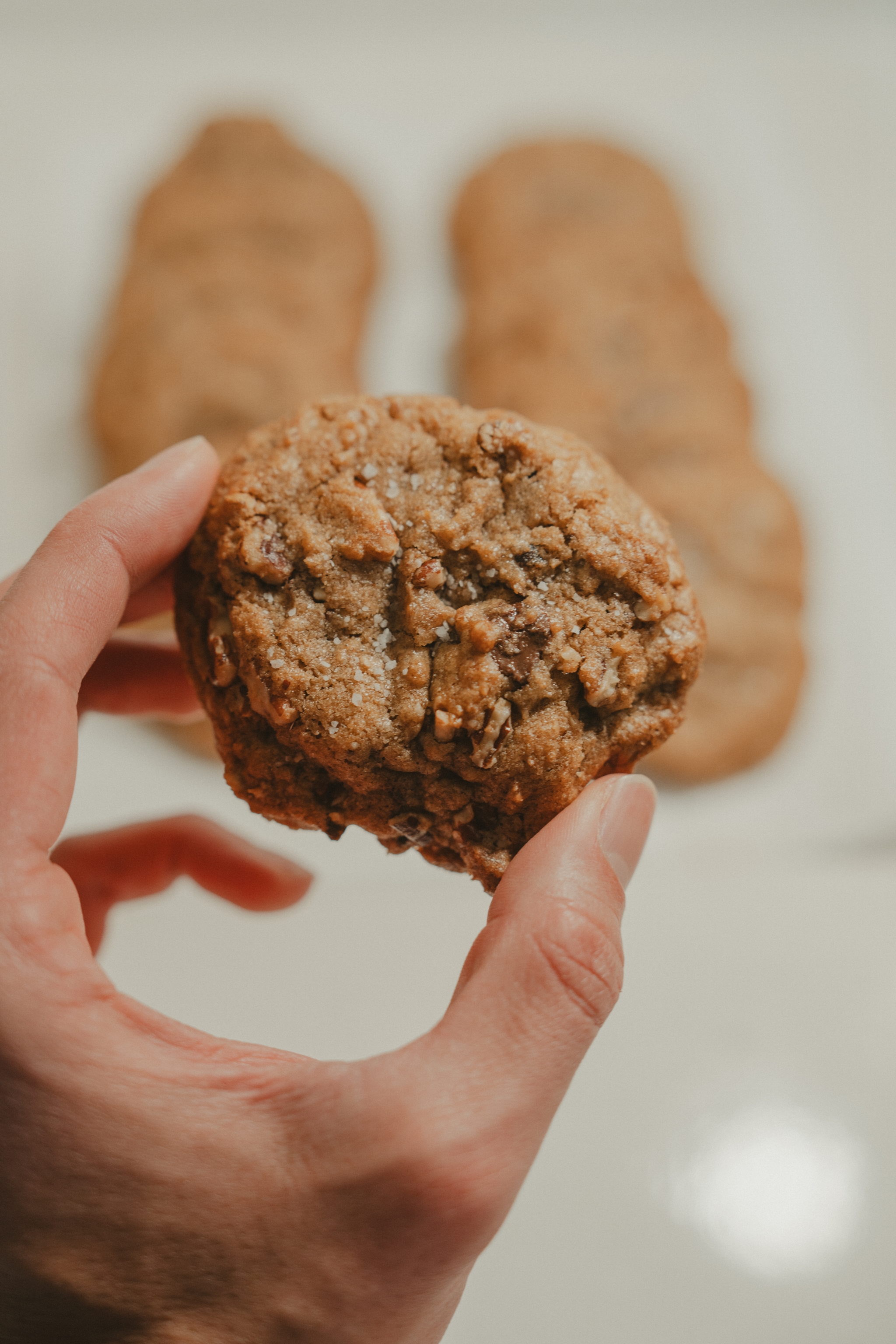 A hand holding a freshly baked cookie with more cookies in the background