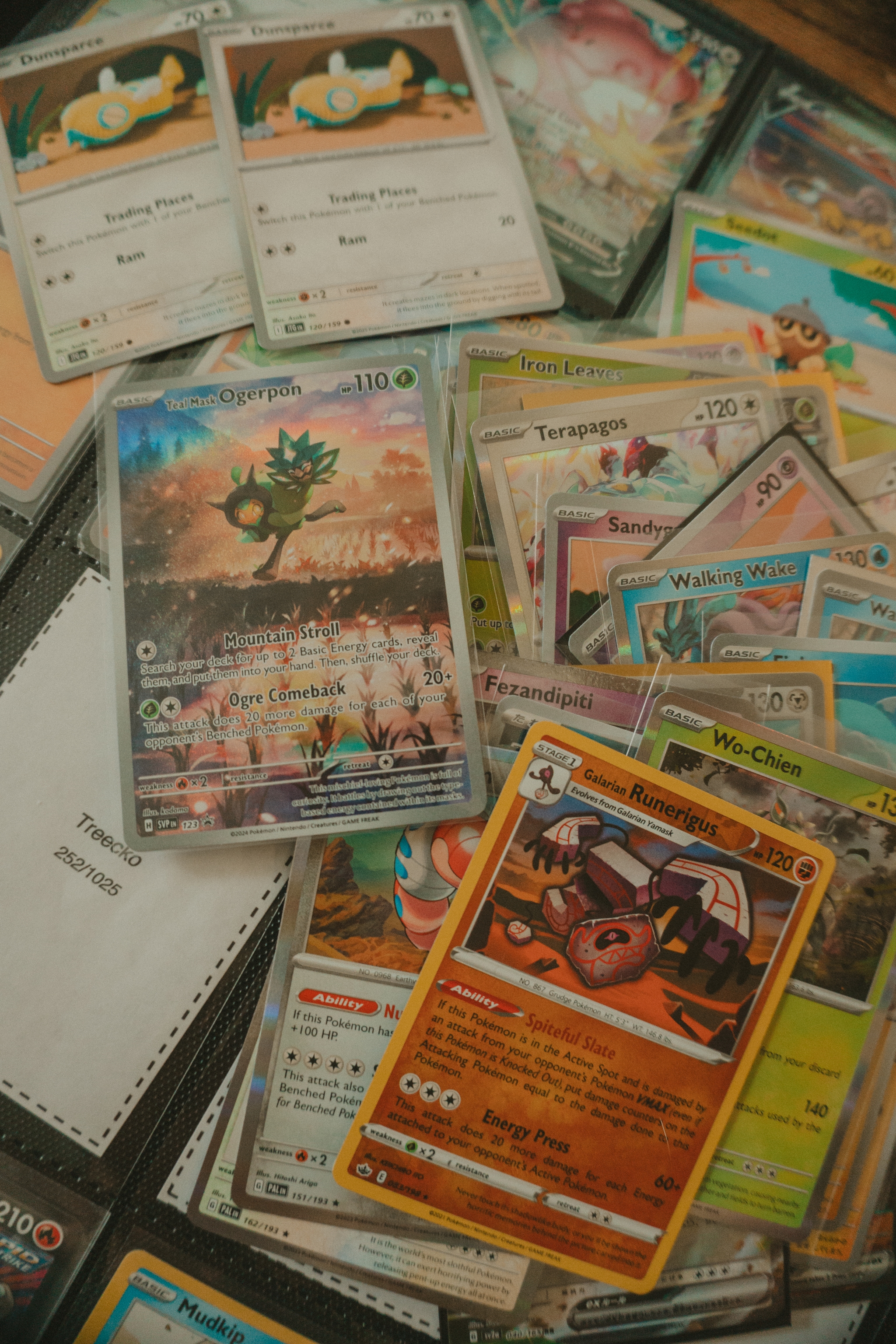 A scattered collection of pokemon trading cards, including some Pokémon cards, displayed loosely and in protective sleeves