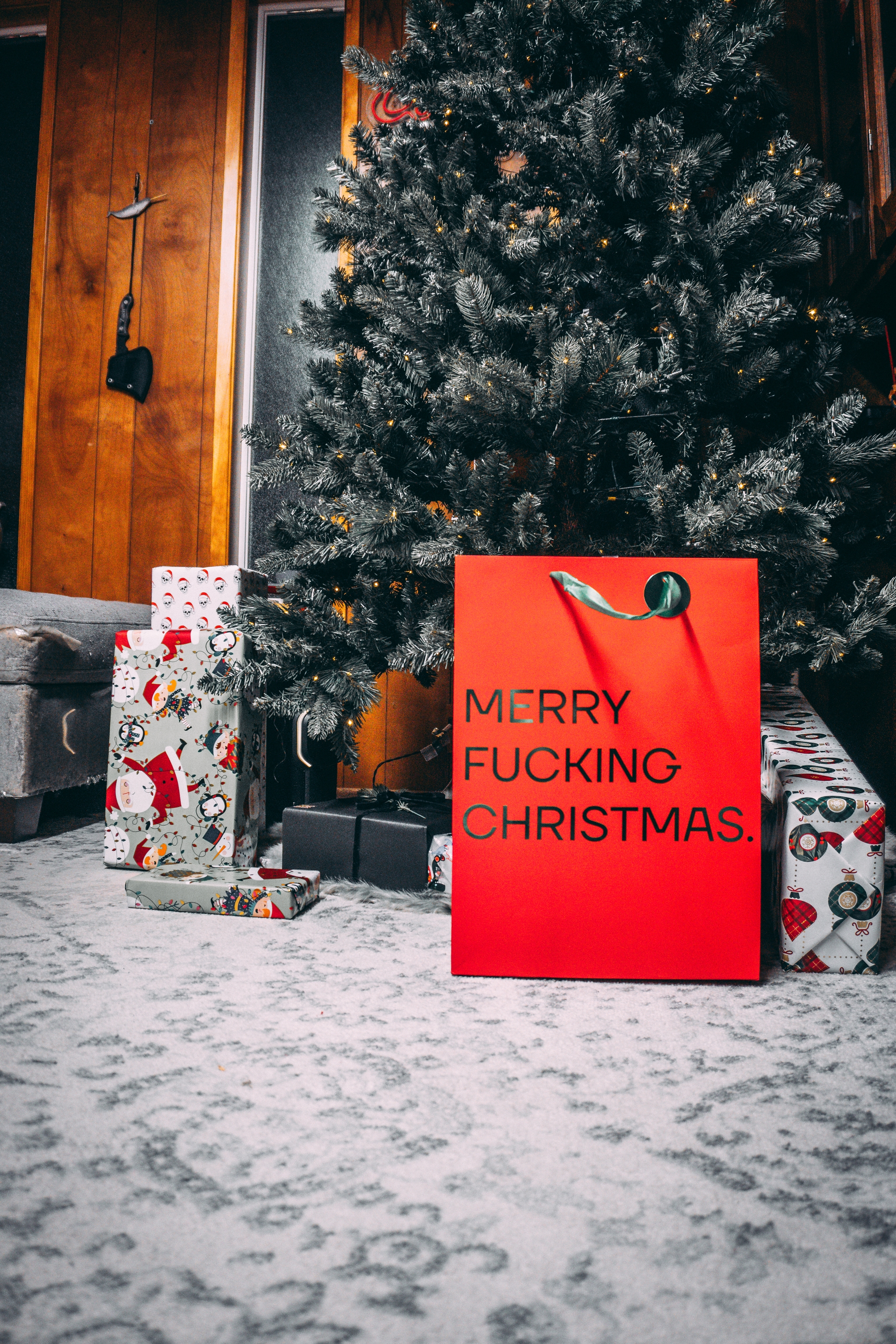 Red gift bag with humorous message by Christmas tree and presents