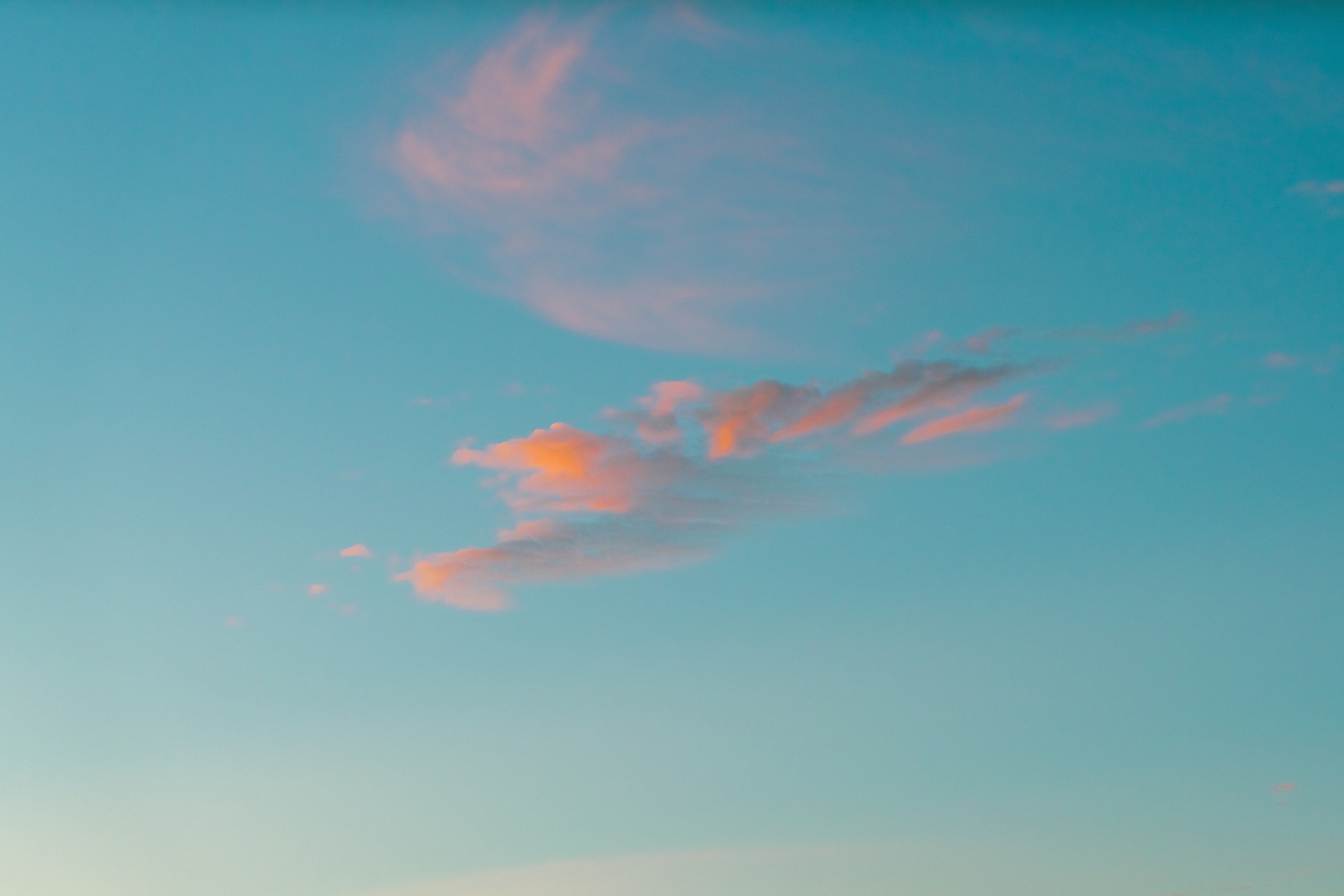 Wispy pink-tinted clouds drifting across a clear blue sky during sunset