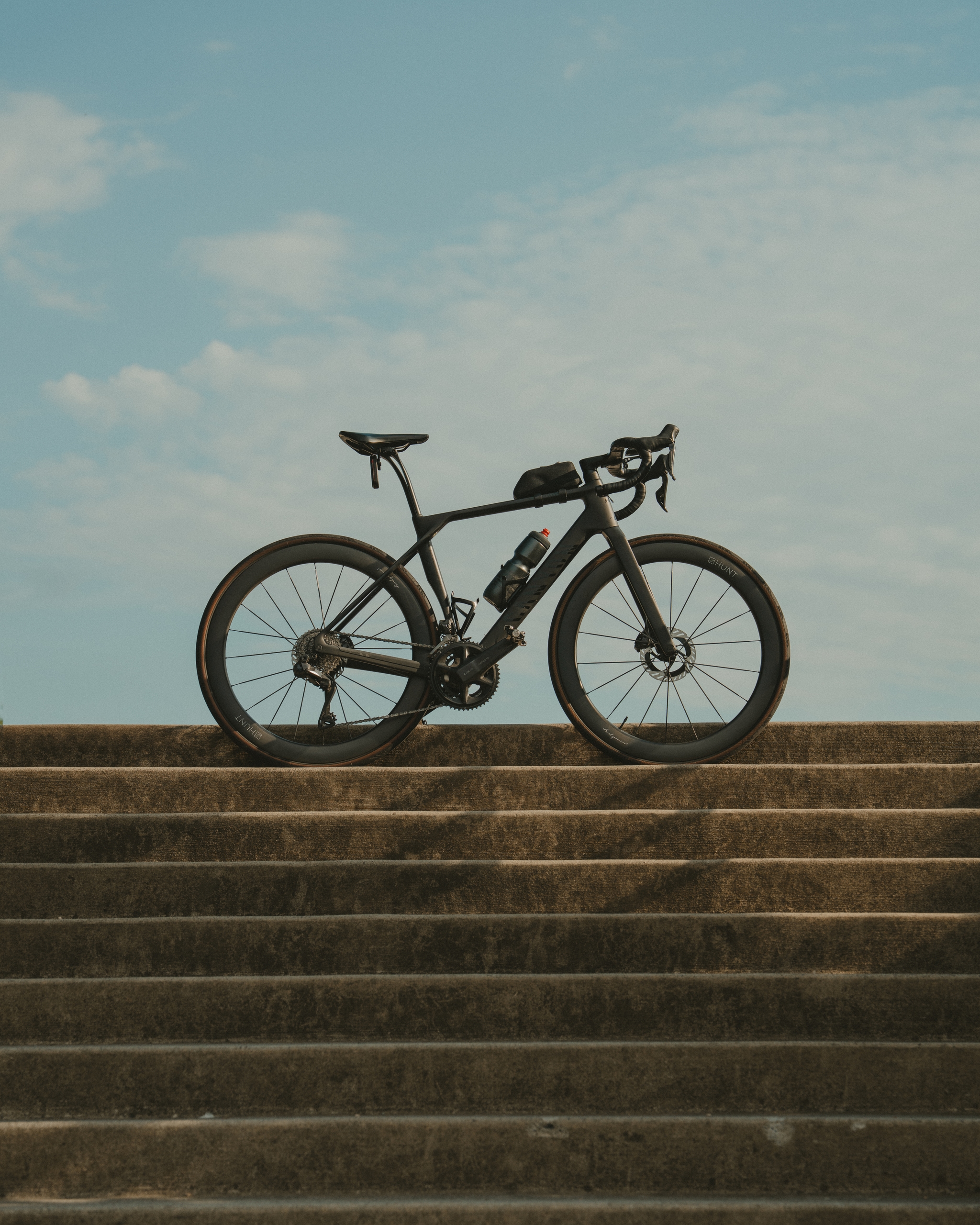 A bicycle is positioned on a set of concrete steps against a backdrop of a partly cloudy sky