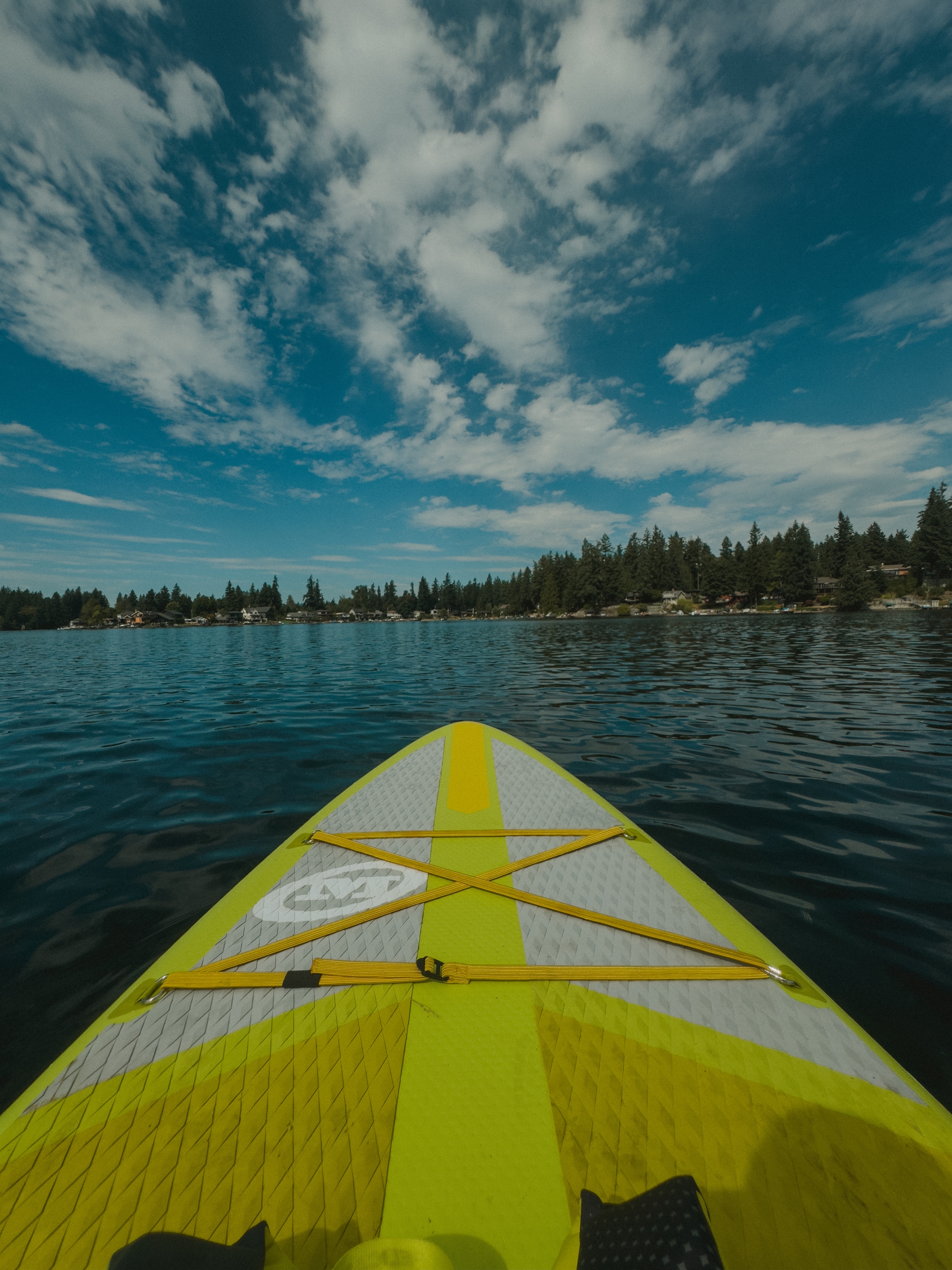 A paddleboard on a calm lake with a view of the shoreline and a sky filled with scattered clouds