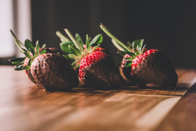 Four strawberries partially dipped in chocolate, arranged on a wooden surface with a soft focus background
