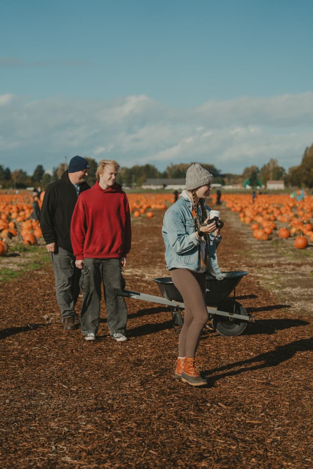 Group at a pumpkin patch with wheelbarrow and pumpkins, under a clear sky