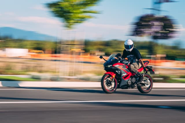 A person wearing a helmet rides a red and black motorcycle at high speed on a road, with a blurred background indicating motion
