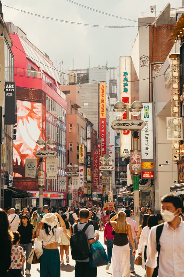A bustling urban street scene with numerous pedestrians, surrounded by tall buildings adorned with colorful signs and advertisements