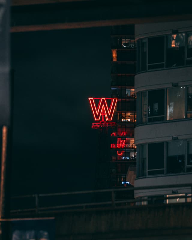A large red neon W sign glows against a dark sky, partially obscured by the corner of a modern building