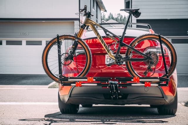 A red car with a bicycle mounted on a rear bike rack, parked in a residential driveway