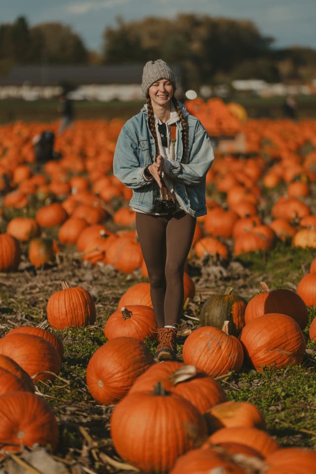 Person walking through a pumpkin patch with a joyful expression, surrounded by orange pumpkins under a clear sky
