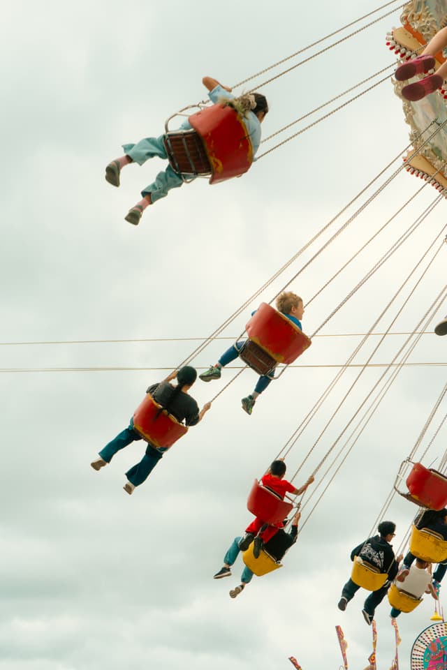 People enjoying a swing ride at an amusement park, suspended high in the air against a cloudy sky