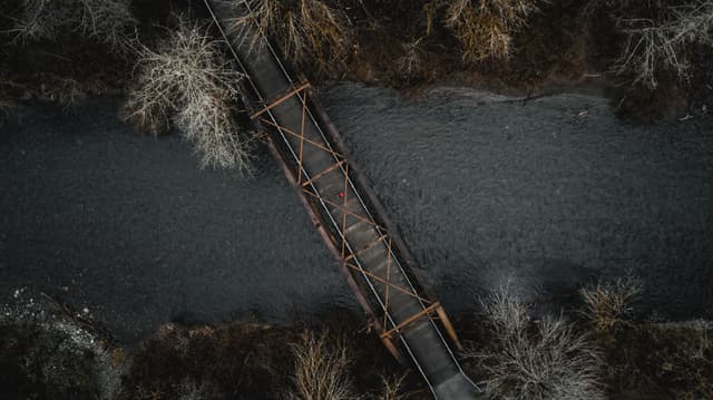 Aerial view of a narrow bridge crossing over a river, surrounded by leafless trees