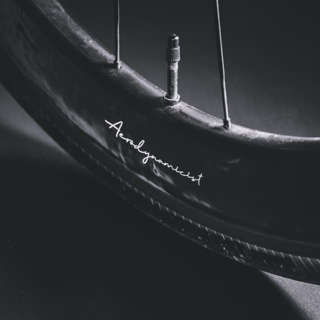 A close-up of a bicycle wheel with a visible valve stem and a signature on the tire