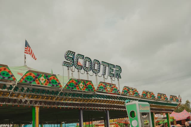 An amusement park ride named Scooter with colorful patterns and an American flag on top. The sky is overcast