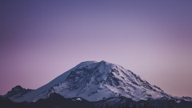 A snow-capped mountain under a purple sky at dusk