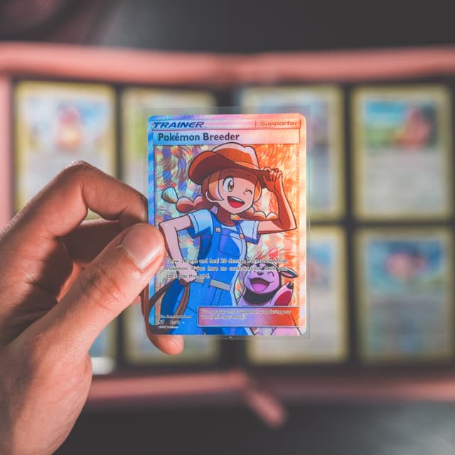 Hand holding a Pokemon trading card with a collection album in the background